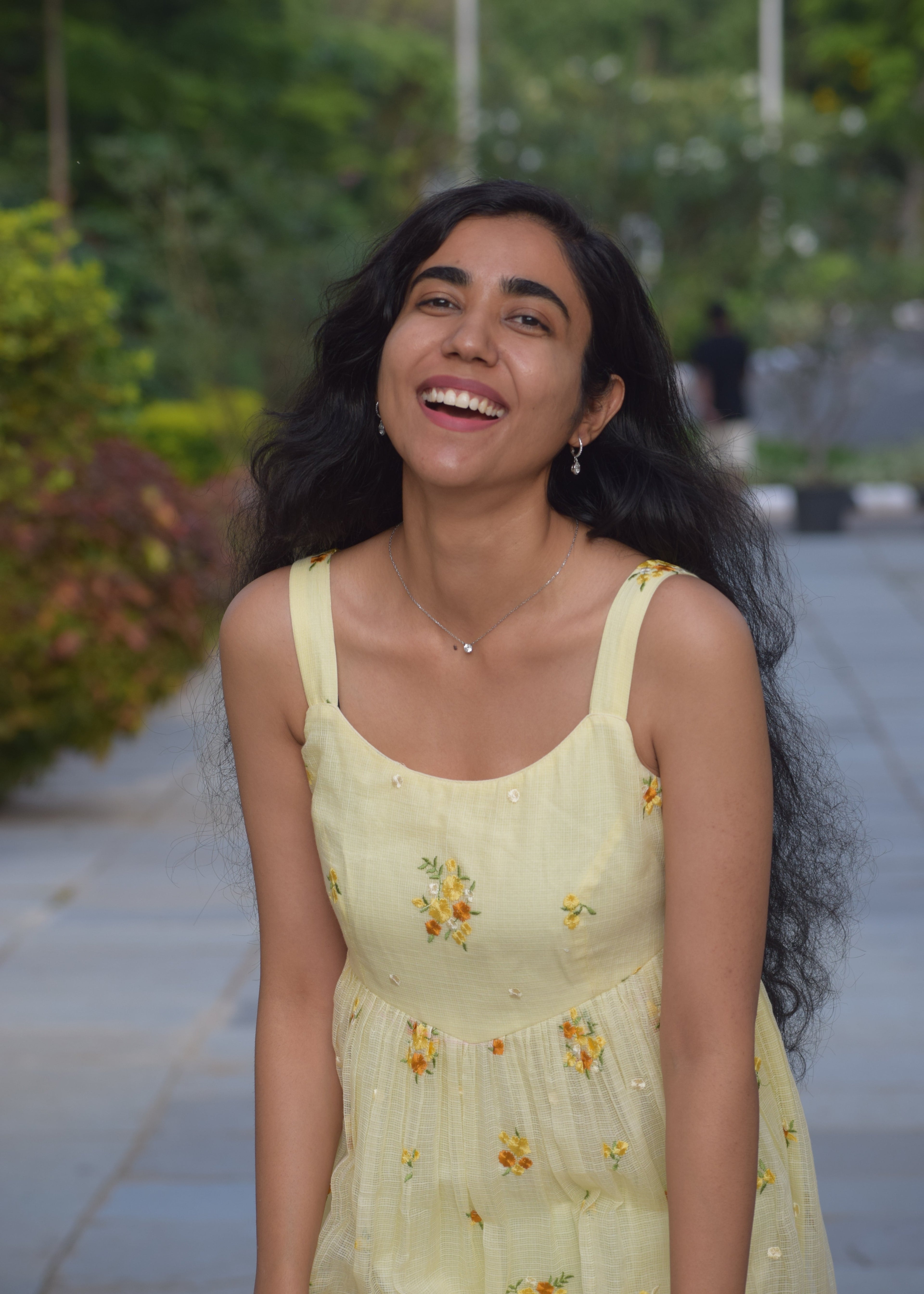 Woman in a yellow dress with floral patterns standing outdoors.
