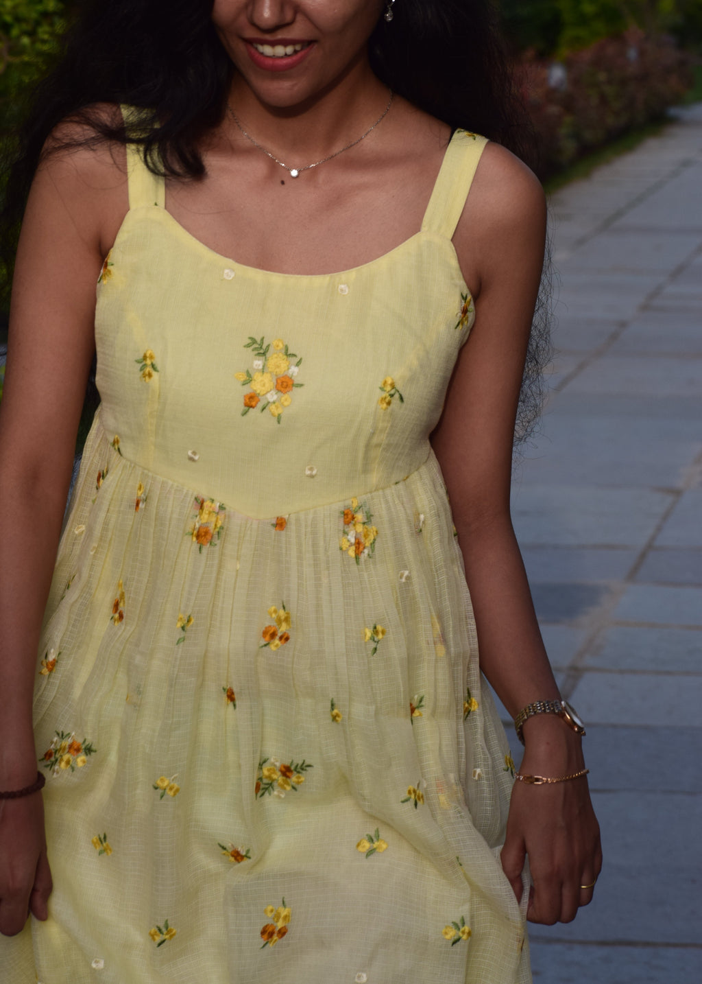 Woman wearing a yellow dress with floral patterns, standing outdoors.
