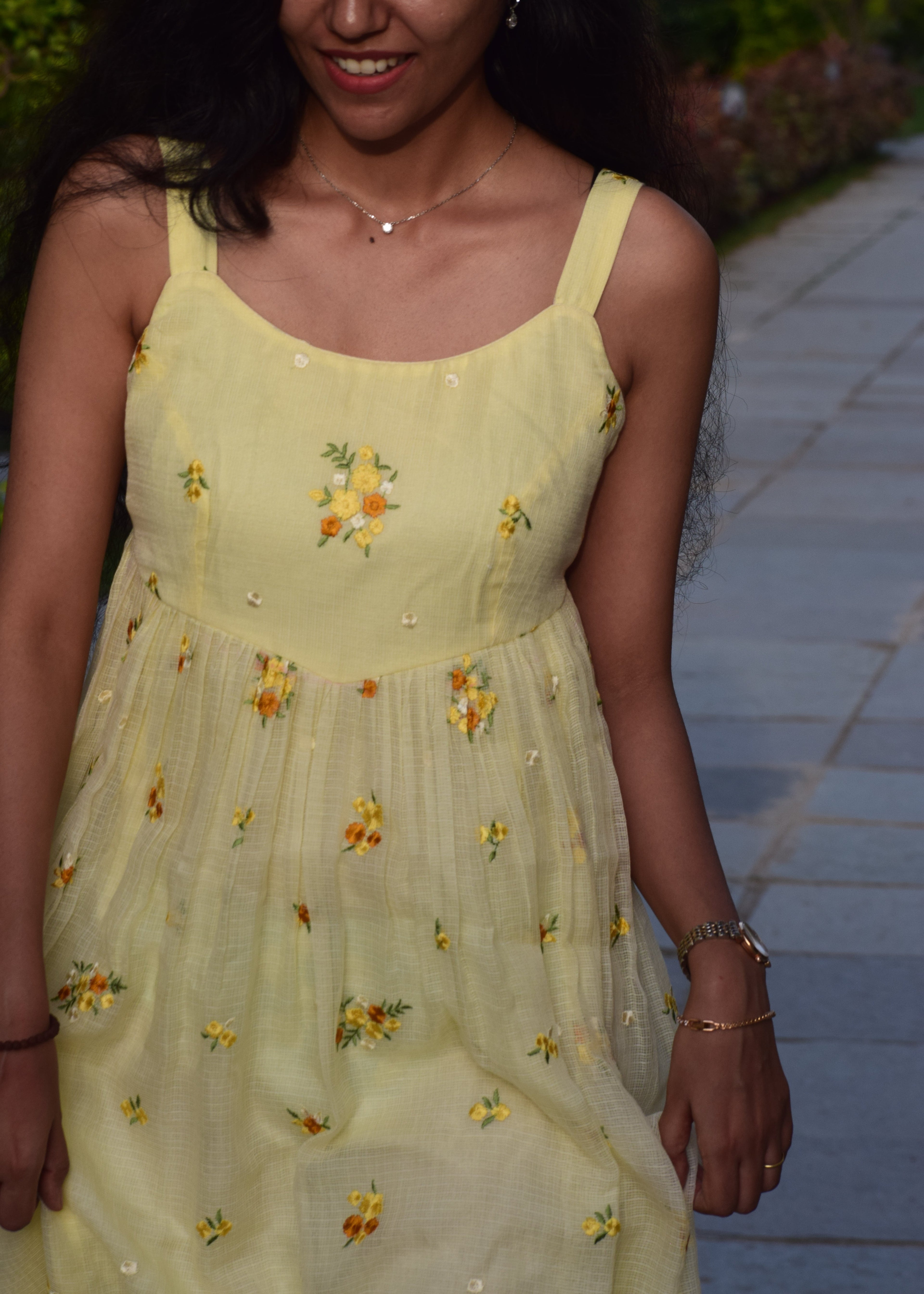Woman wearing a yellow dress with floral patterns, standing outdoors.