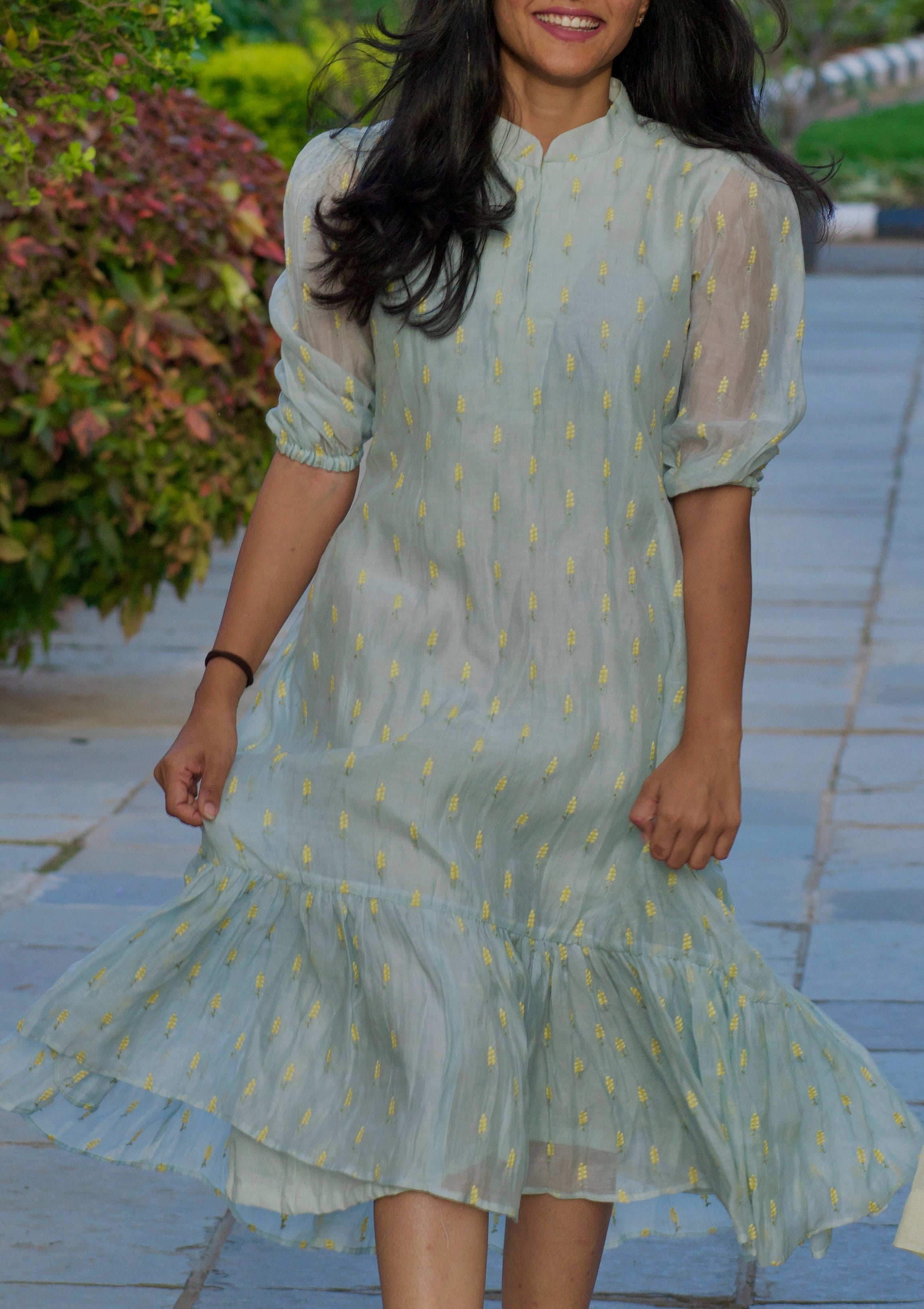 Two women in light green dresses standing on a stone path with greenery in the background