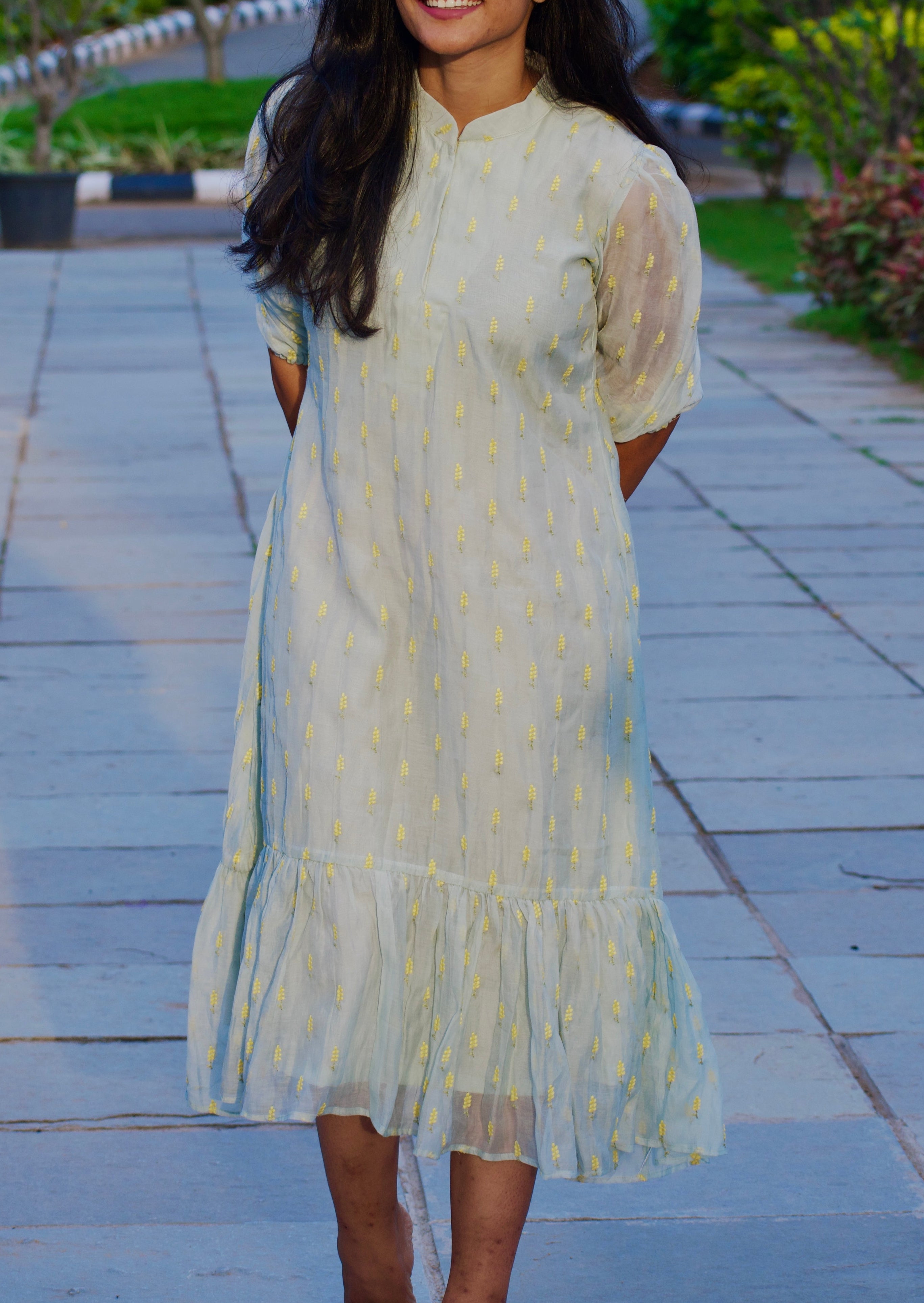 Woman in a light dress standing on a paved path with greenery in the background