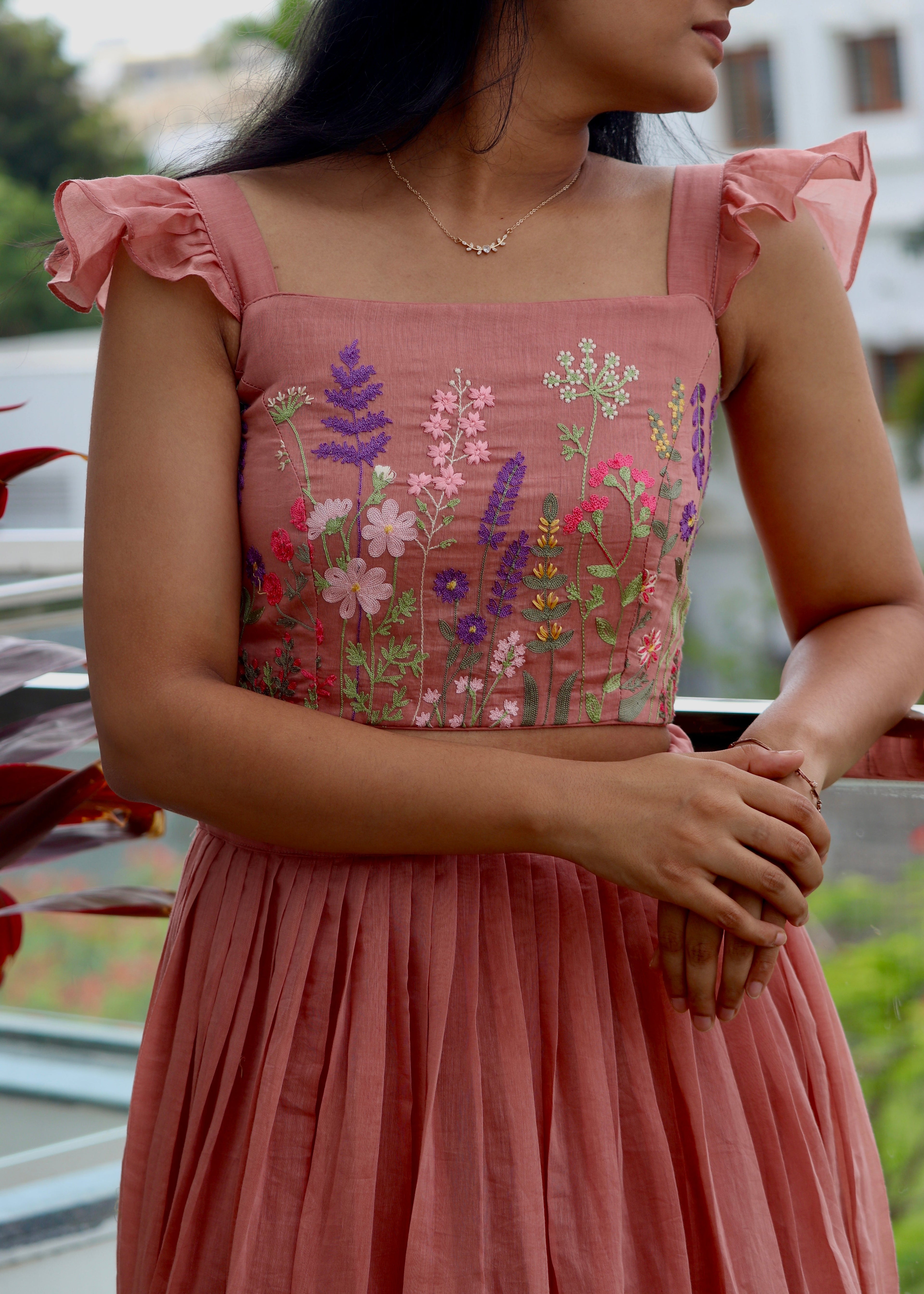 Woman wearing a pink embroidered top and pleated skirt with blurred background