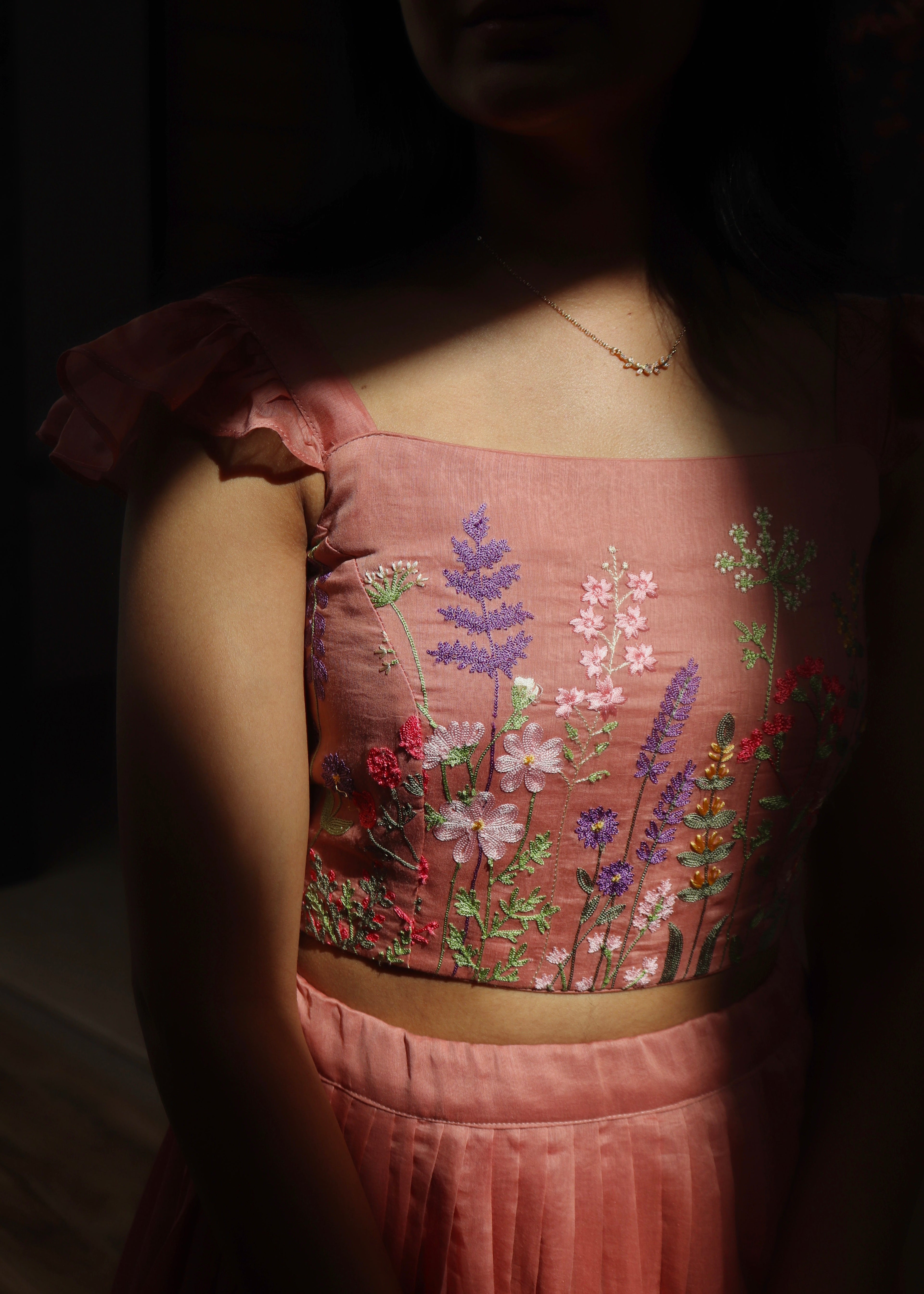 Person wearing a pink embroidered top with floral patterns in a dimly lit setting