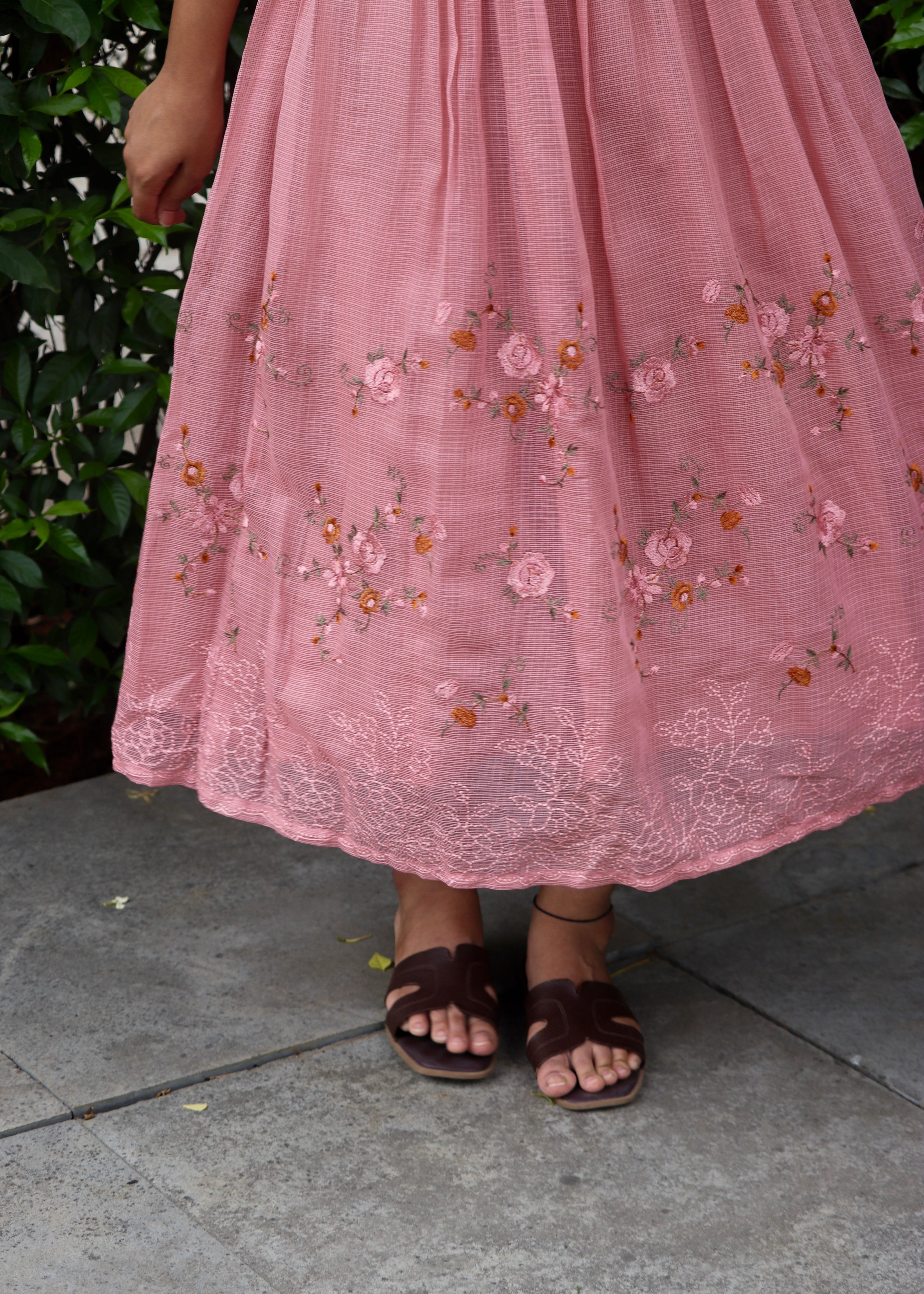 Person wearing a pink embroidered dress standing on a stone pavement.