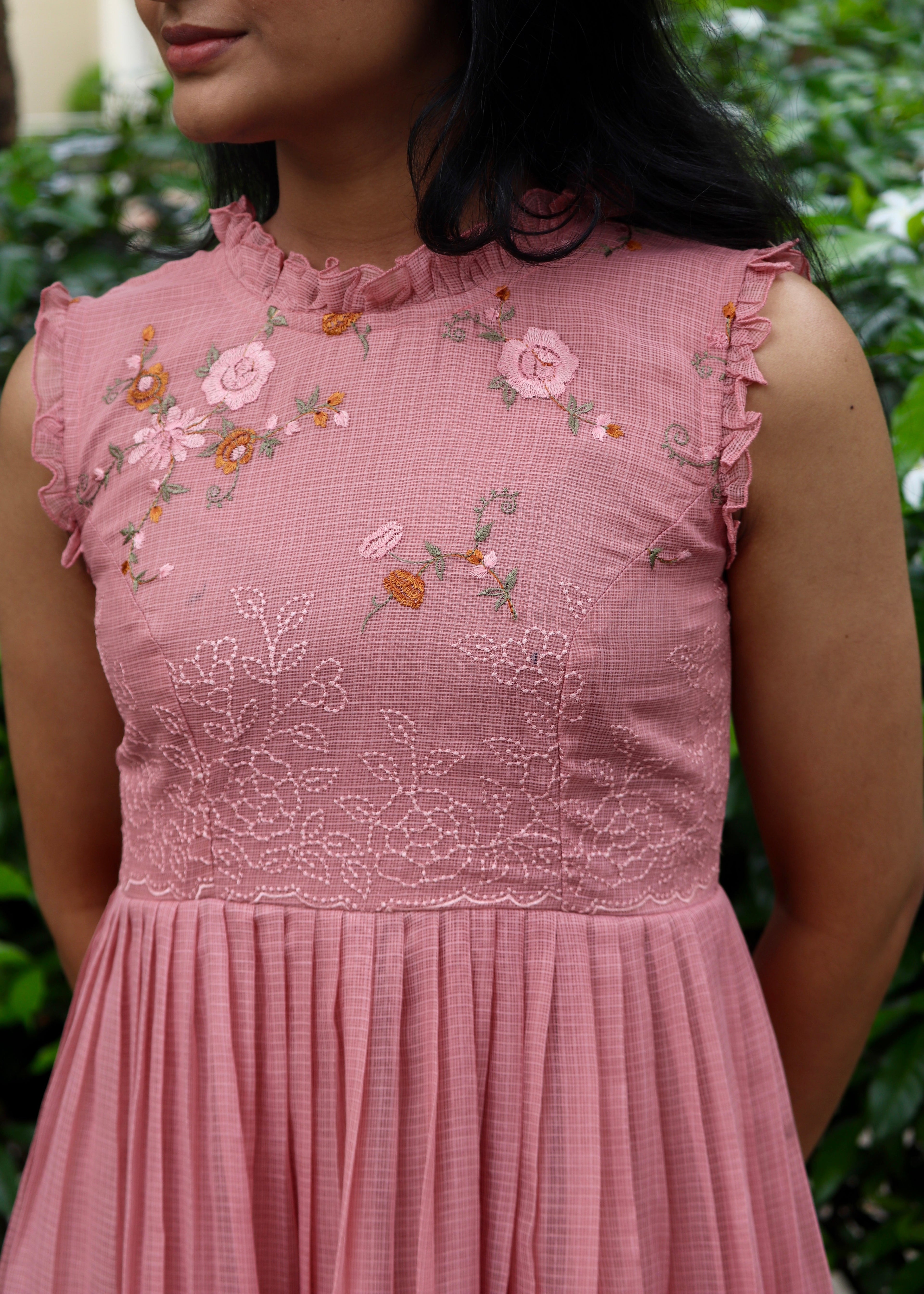 Woman wearing a pink dress with floral embroidery against a blurred green background