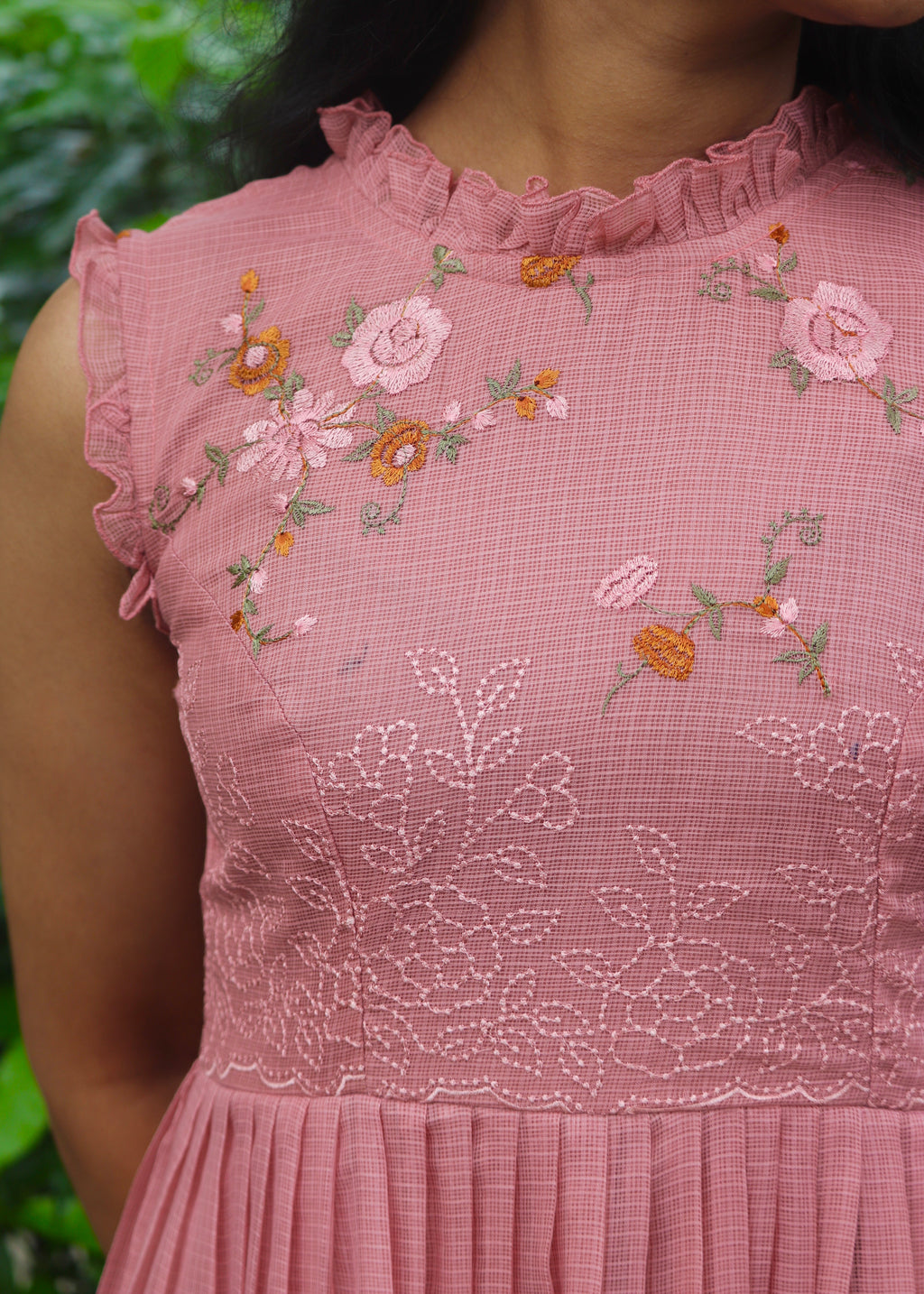 Close-up of a pink dress with floral embroidery against a blurred green background