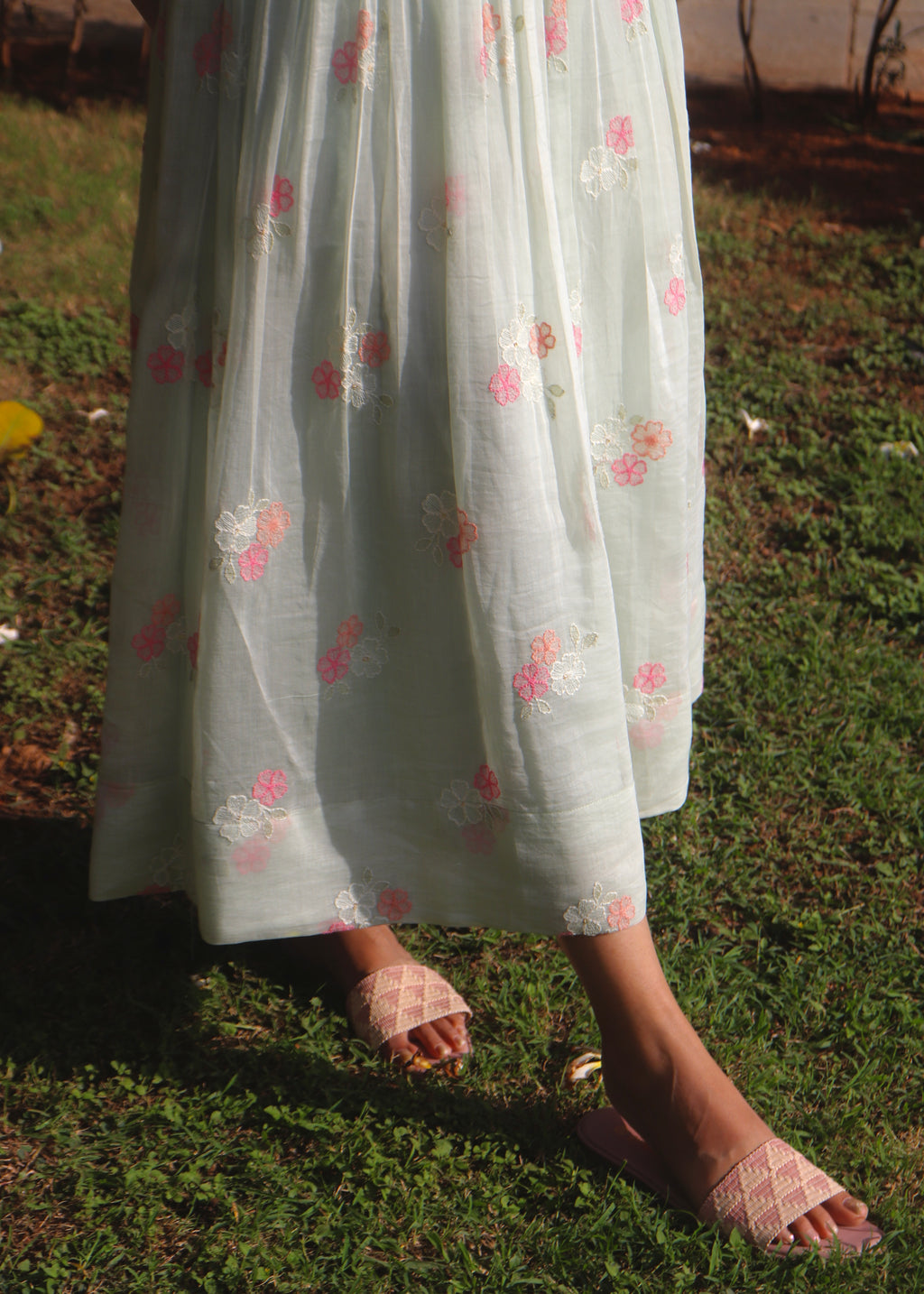 Person wearing a light-colored dress with floral patterns standing on grass.