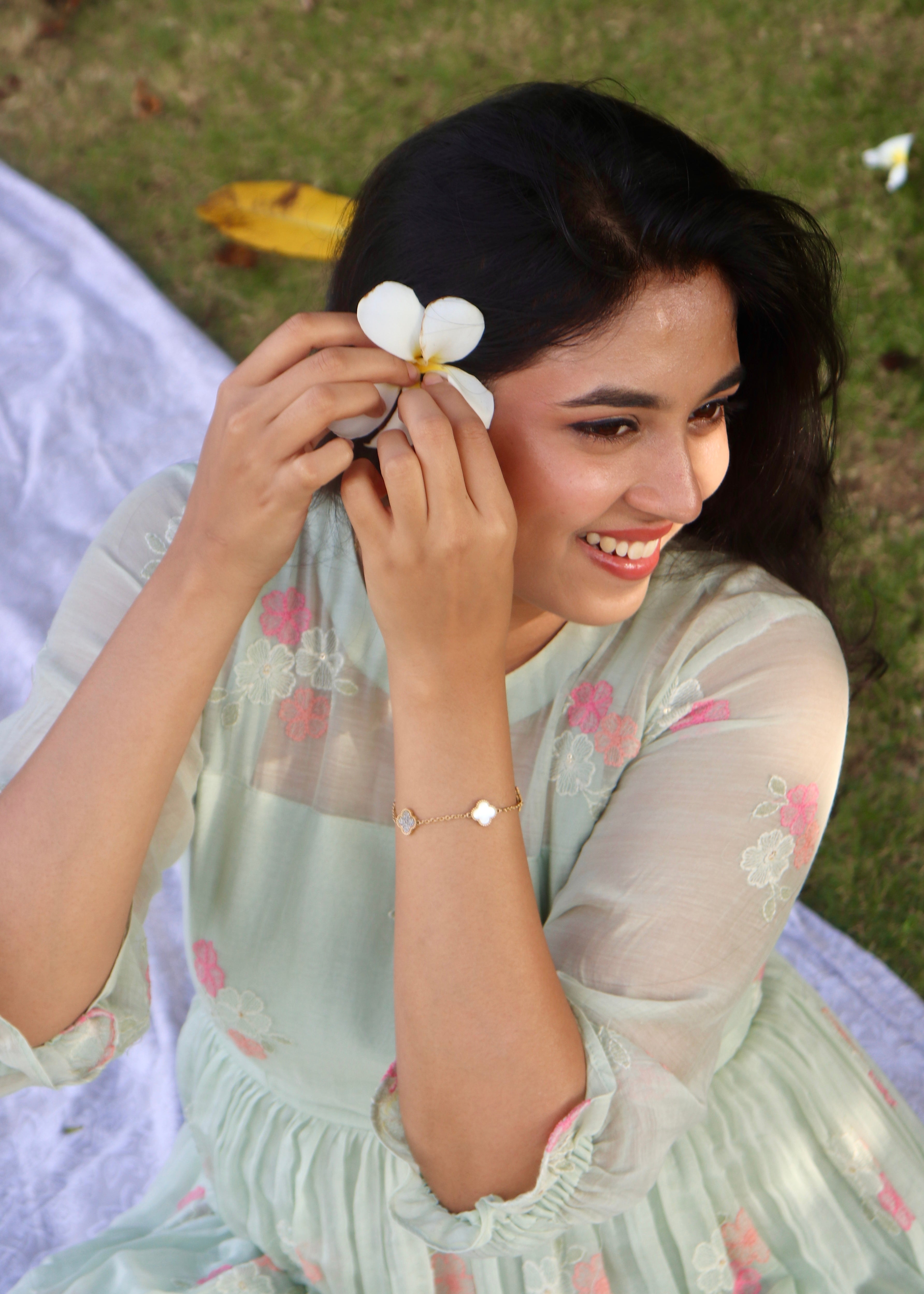 Woman in a light green dress with floral patterns, holding a white flower outdoors.