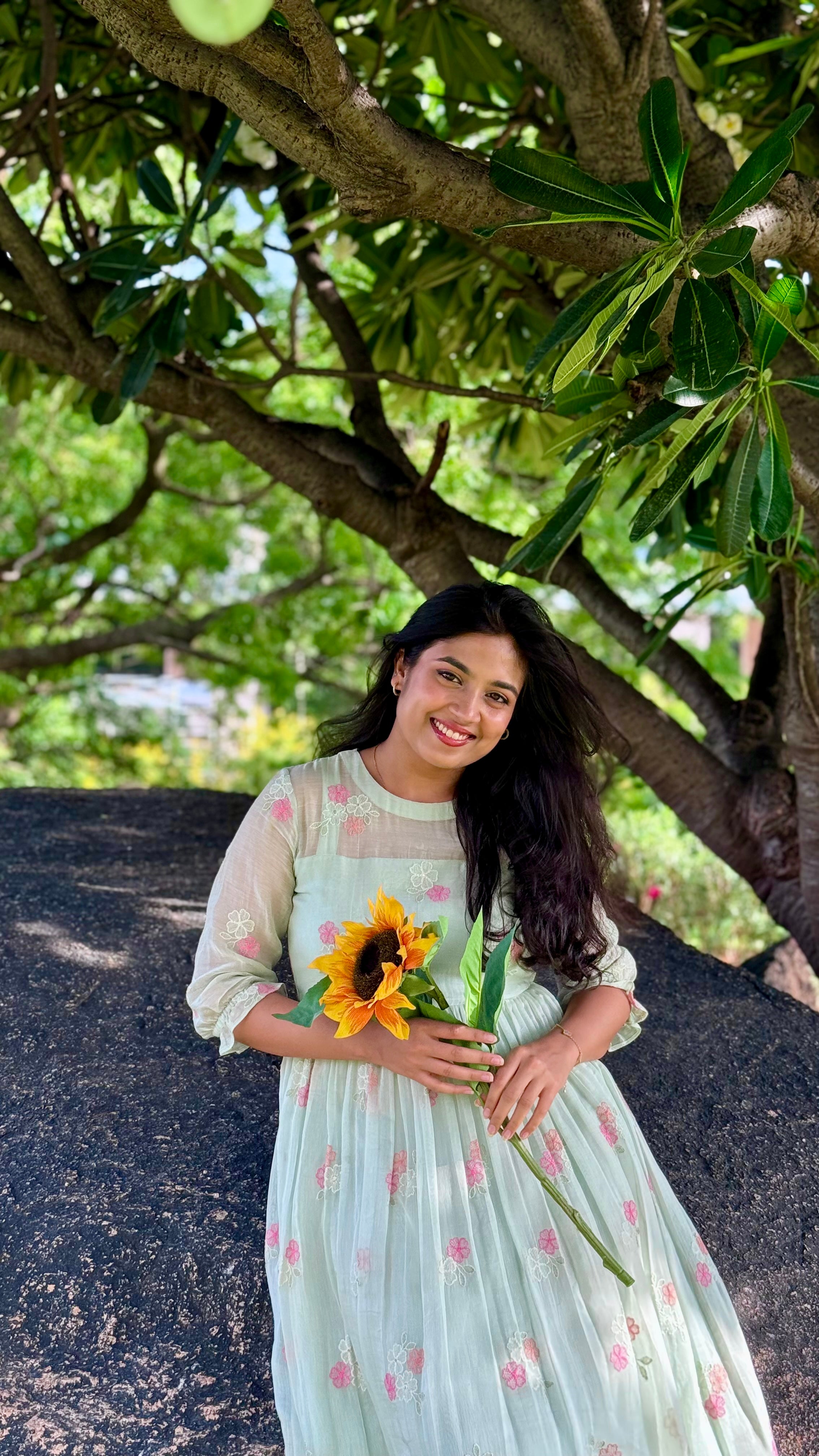 Woman holding a sunflower under a tree