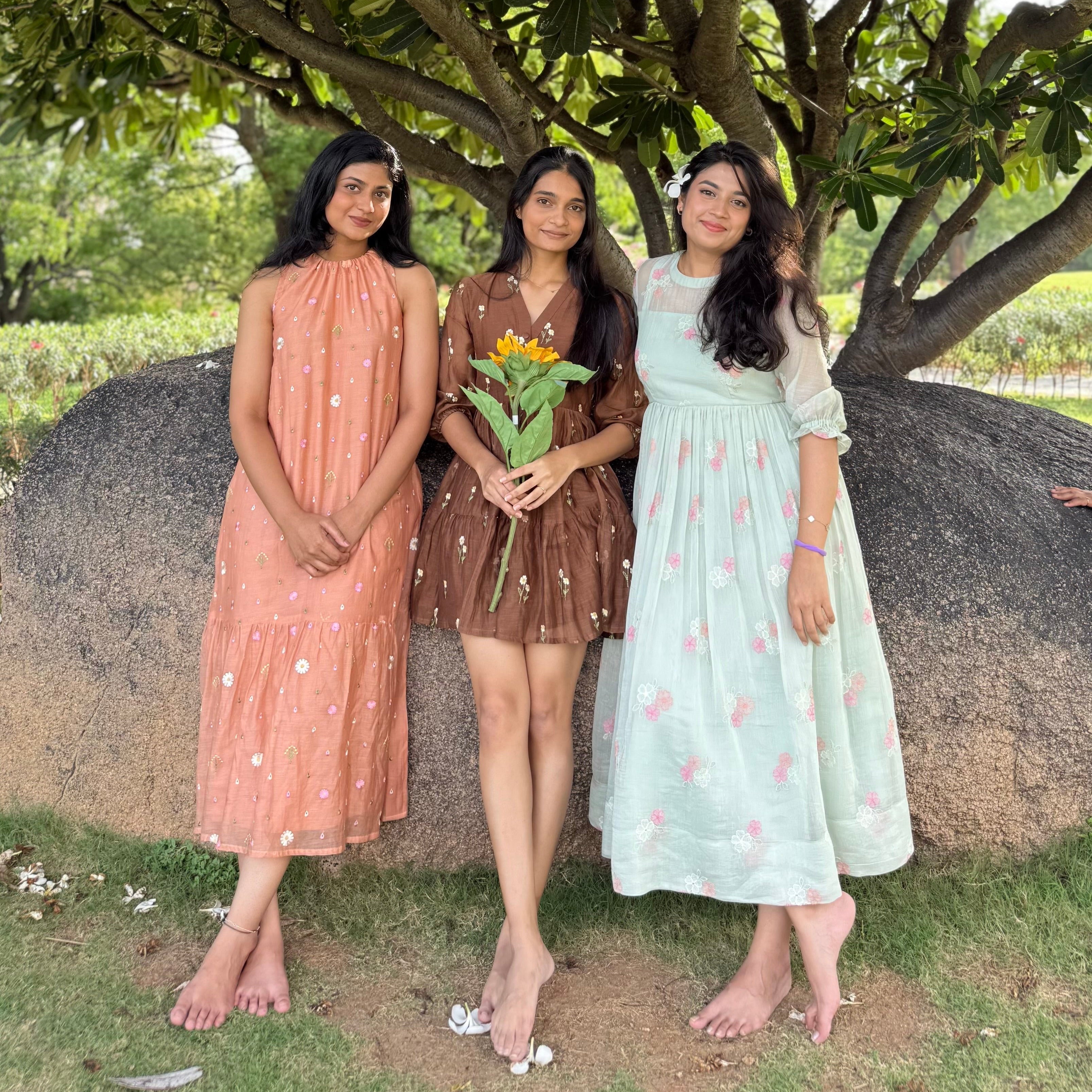 Three women standing under a large tree, wearing dresses.