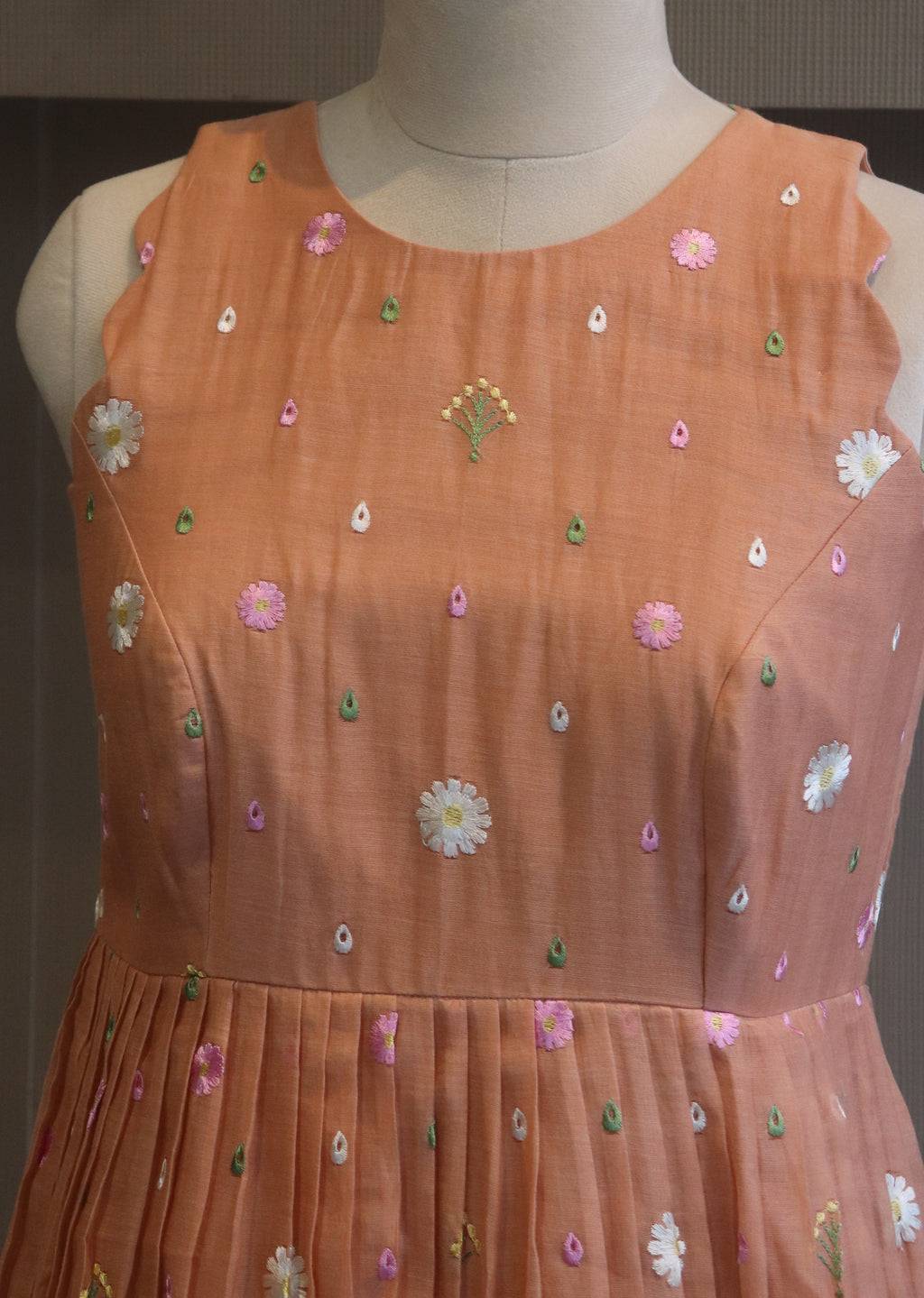 Mannequin wearing a peach-colored dress with floral embroidery on a dark background