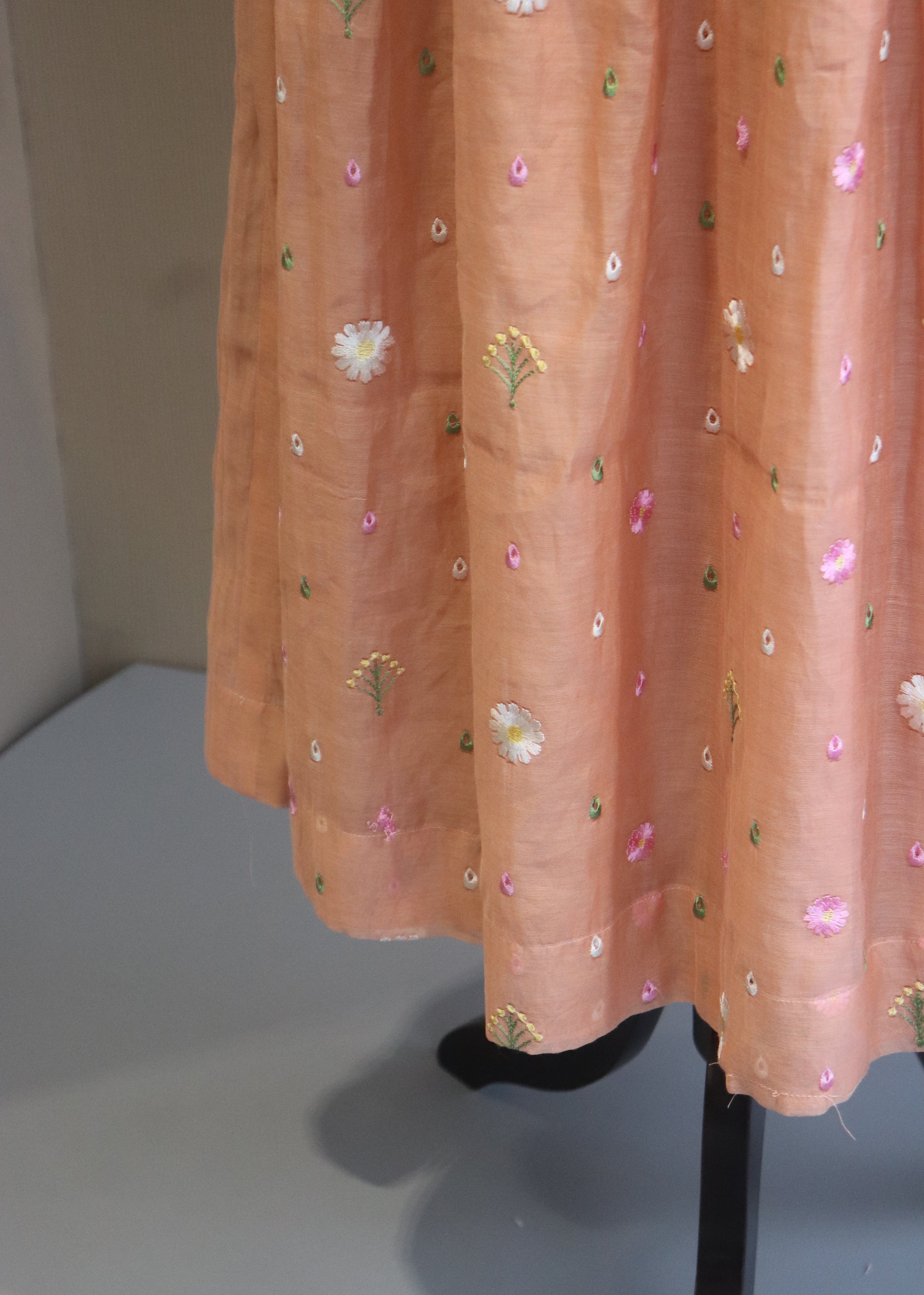 Peach-colored fabric with floral embroidery on a light gray background