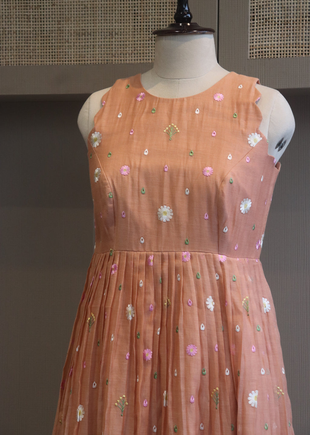Peach-colored dress with floral patterns on a mannequin against a neutral background