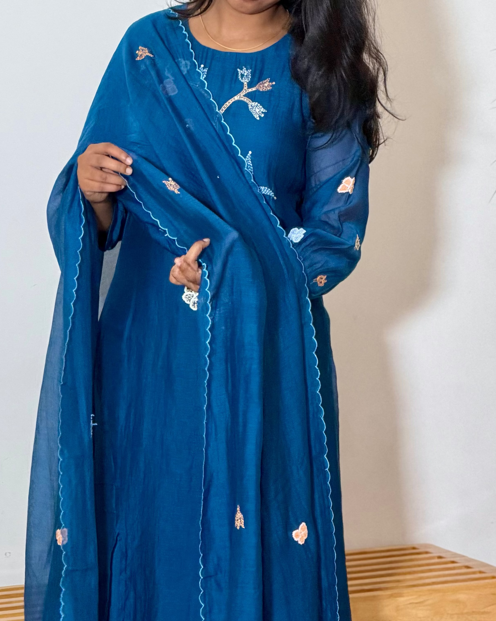 Woman wearing a blue traditional outfit with a matching dupatta in a minimalistic room.