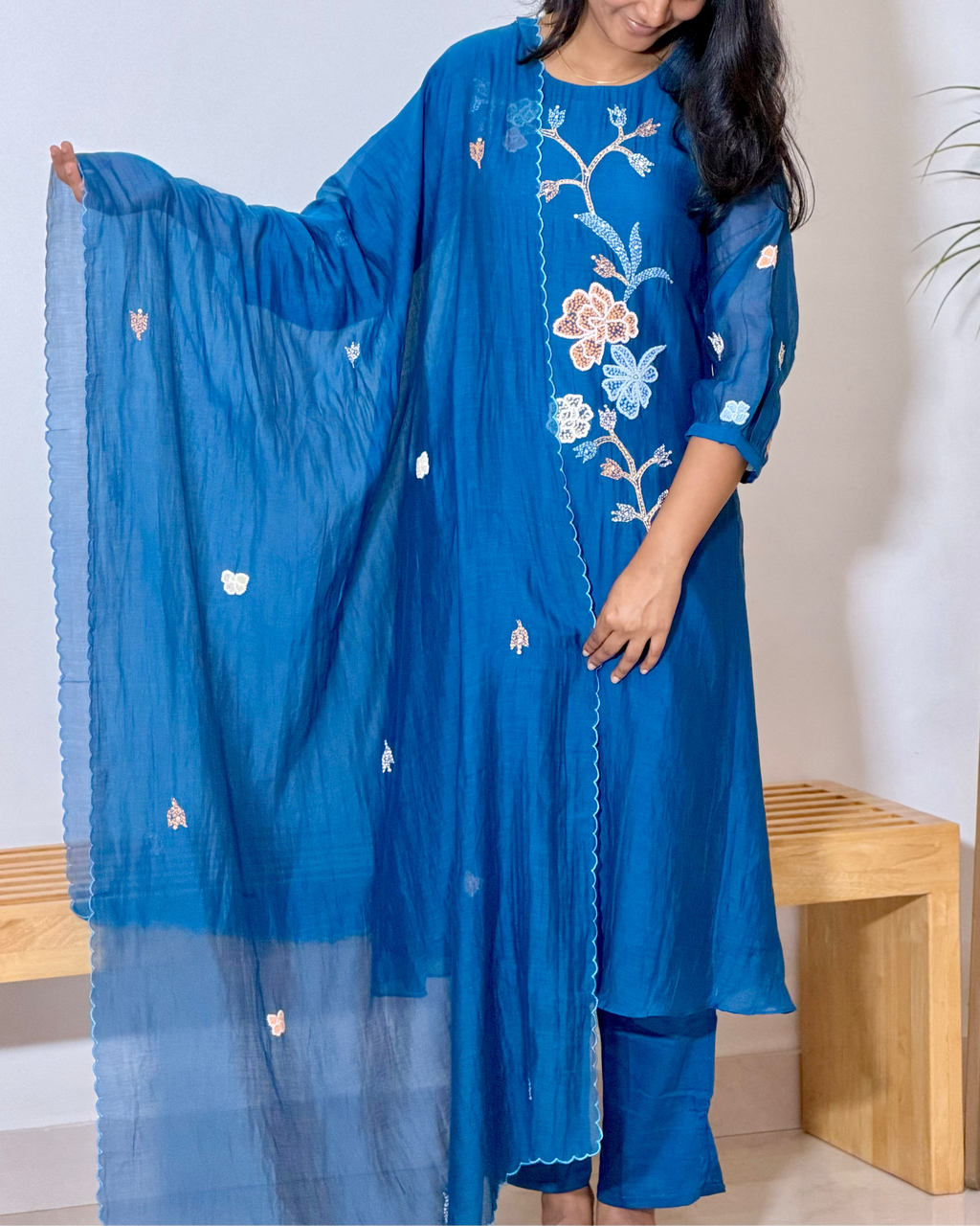Woman wearing a blue embroidered outfit with a matching dupatta, standing indoors.