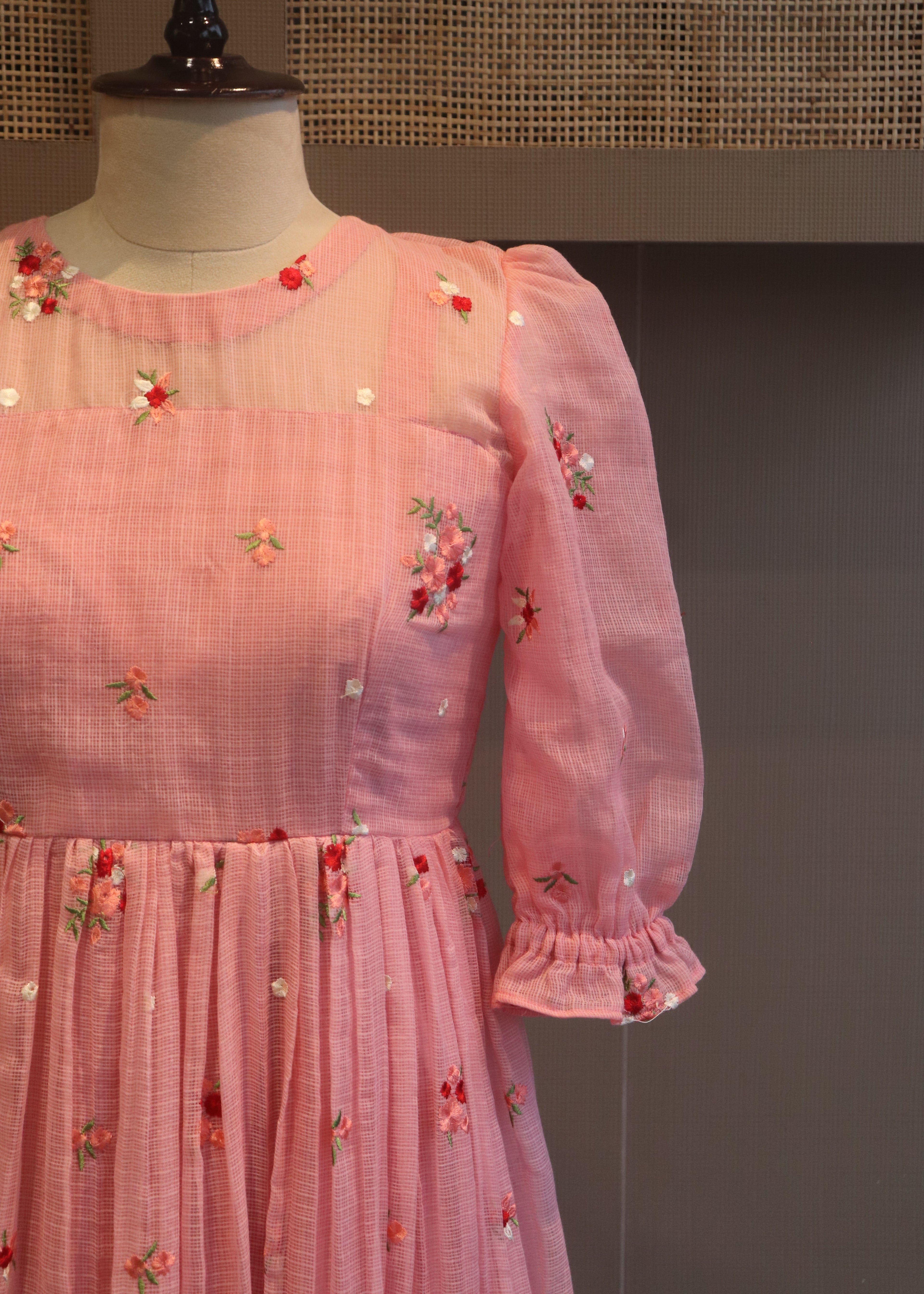 Pink blouse with floral embroidery on a mannequin against a dark background