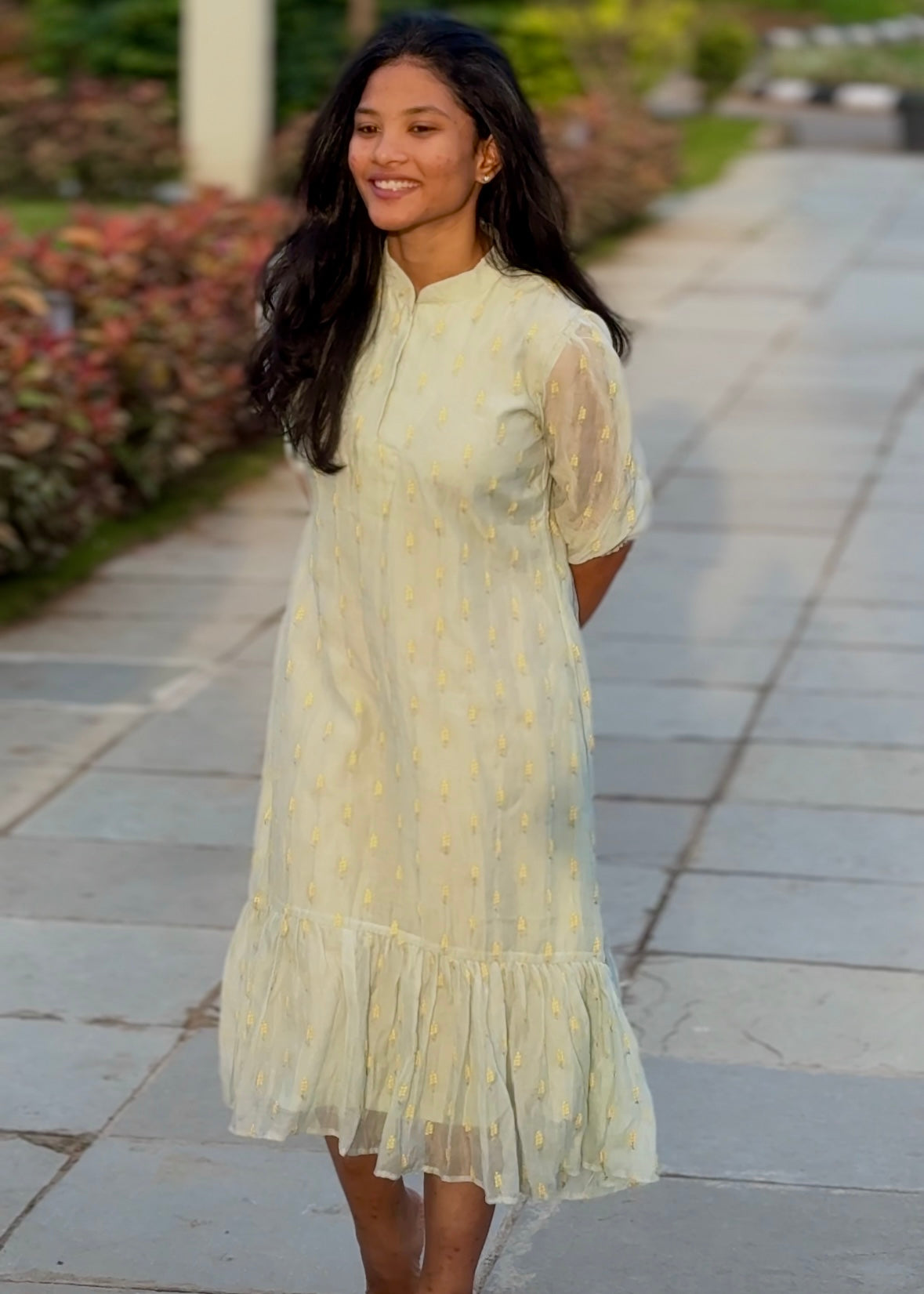 Woman in a light yellow dress standing on a stone path with greenery in the background