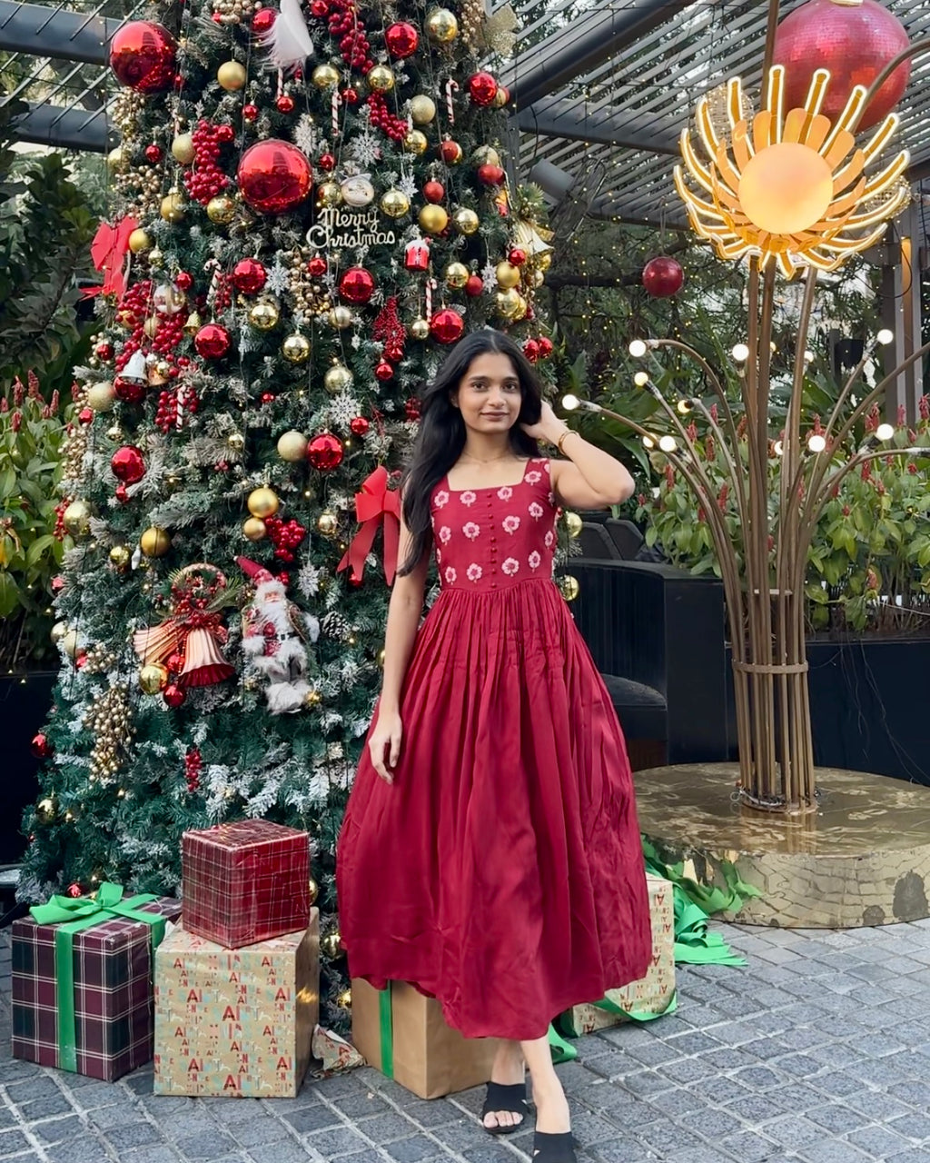 Woman in a red dress standing in front of a Christmas tree with decorations and presents.