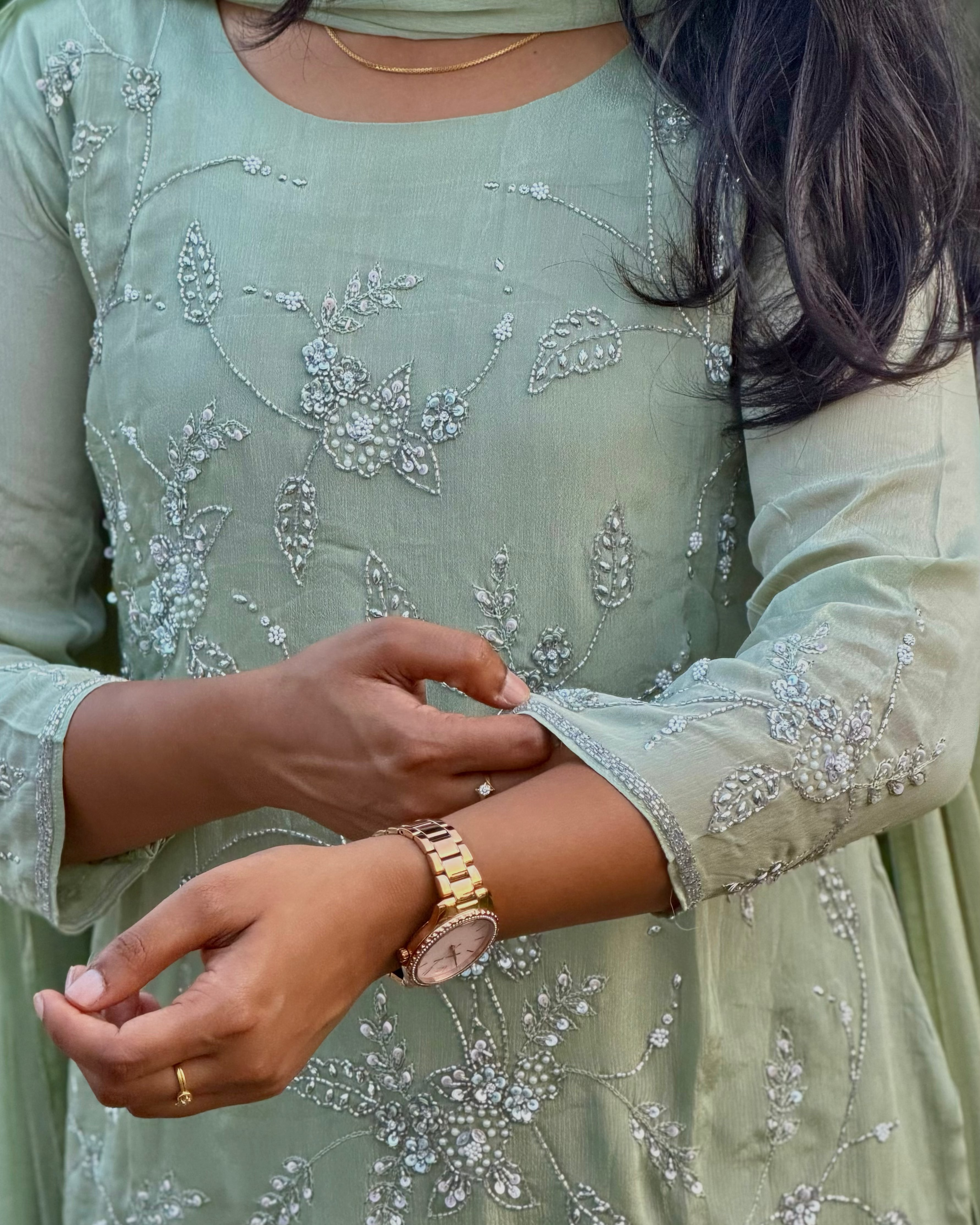 Person wearing a light green embroidered outfit with a gold watch on wrist.