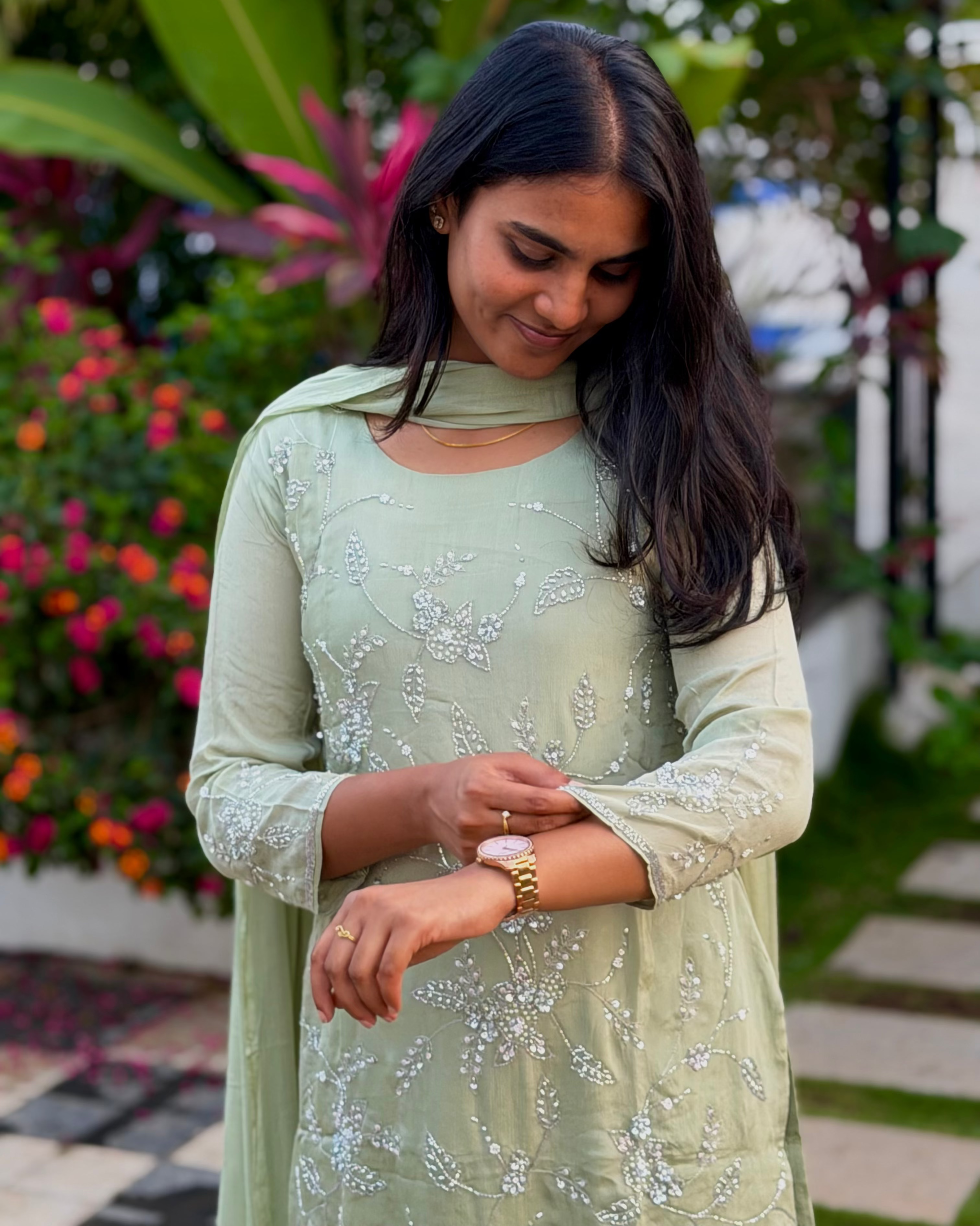 Woman wearing a light green traditional outfit with floral patterns in an outdoor setting.