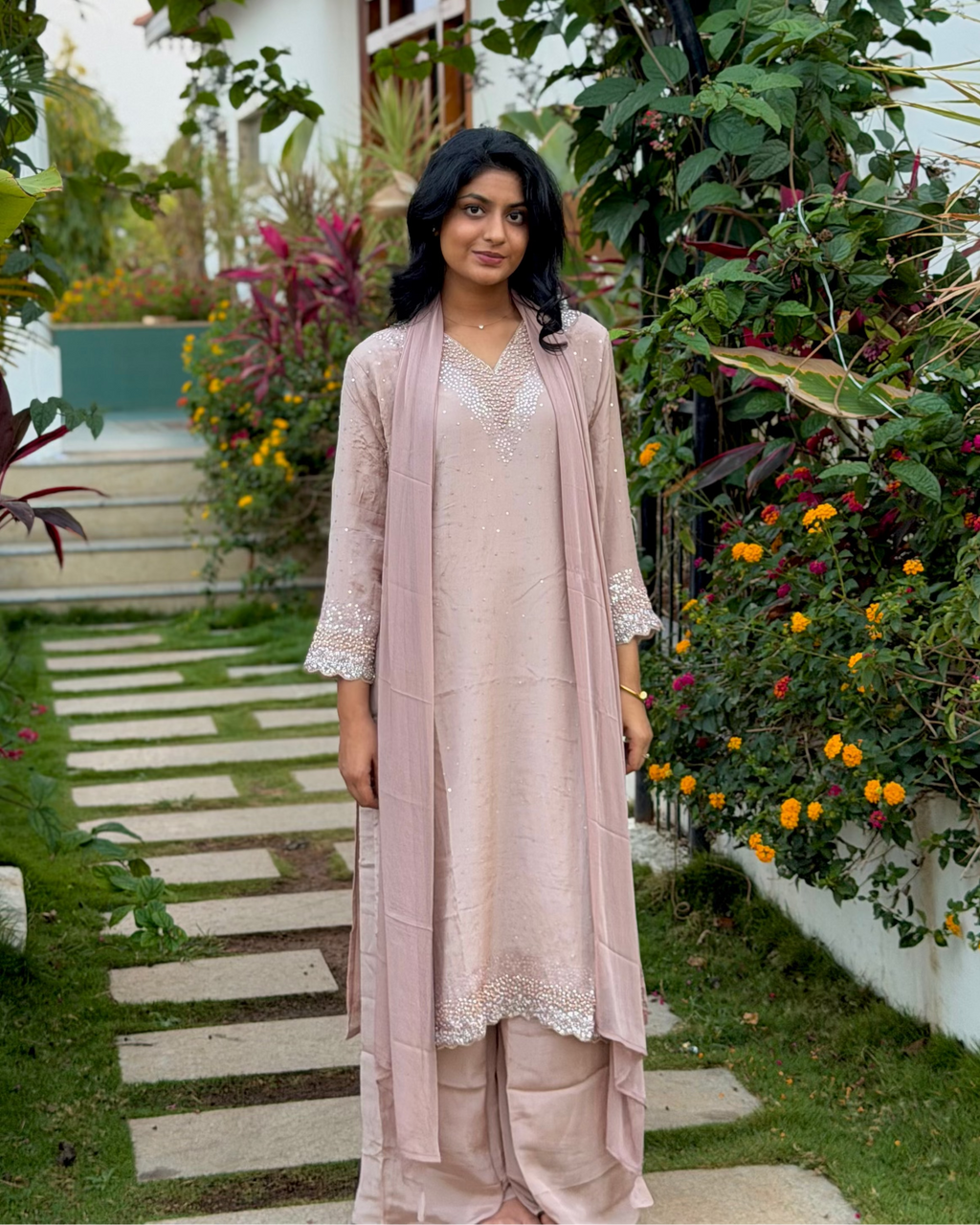Woman in a pink dress standing in a garden with plants and flowers.