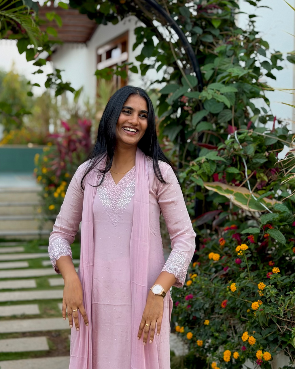 Woman in a pink outfit standing in a garden with greenery and flowers.