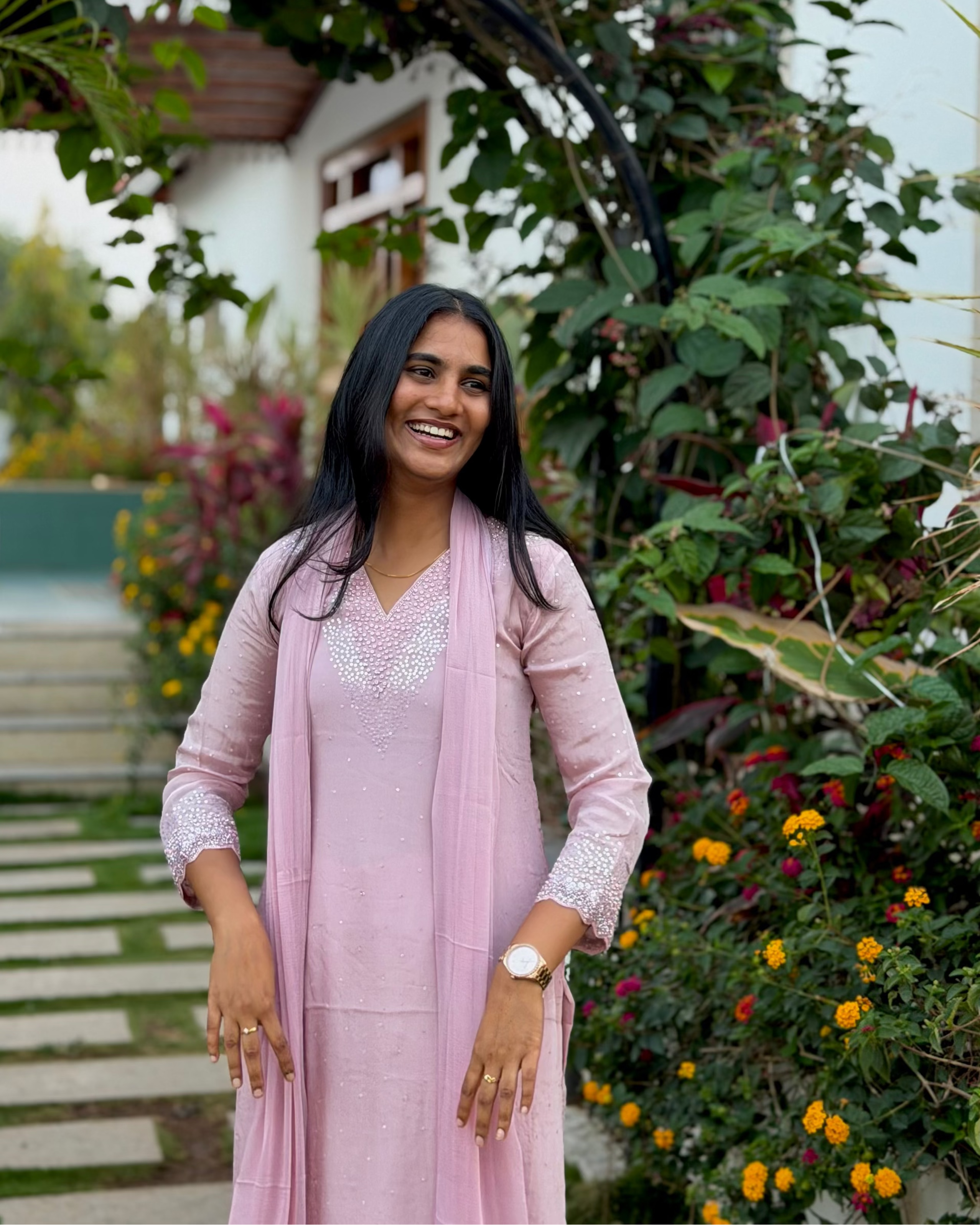 Woman in a pink outfit standing in a garden with greenery and flowers.