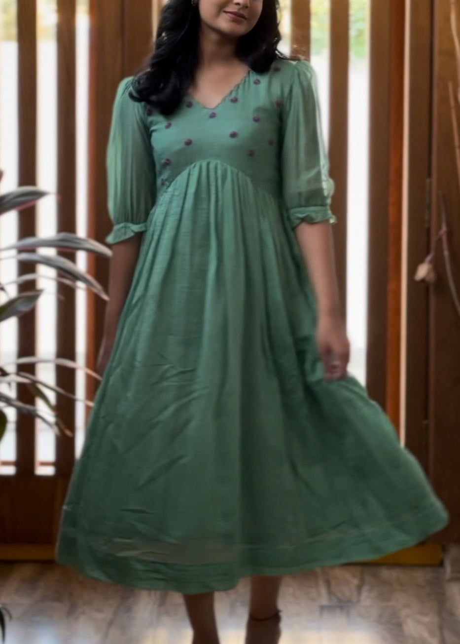 Woman wearing a green dress with a subtle pattern indoors.