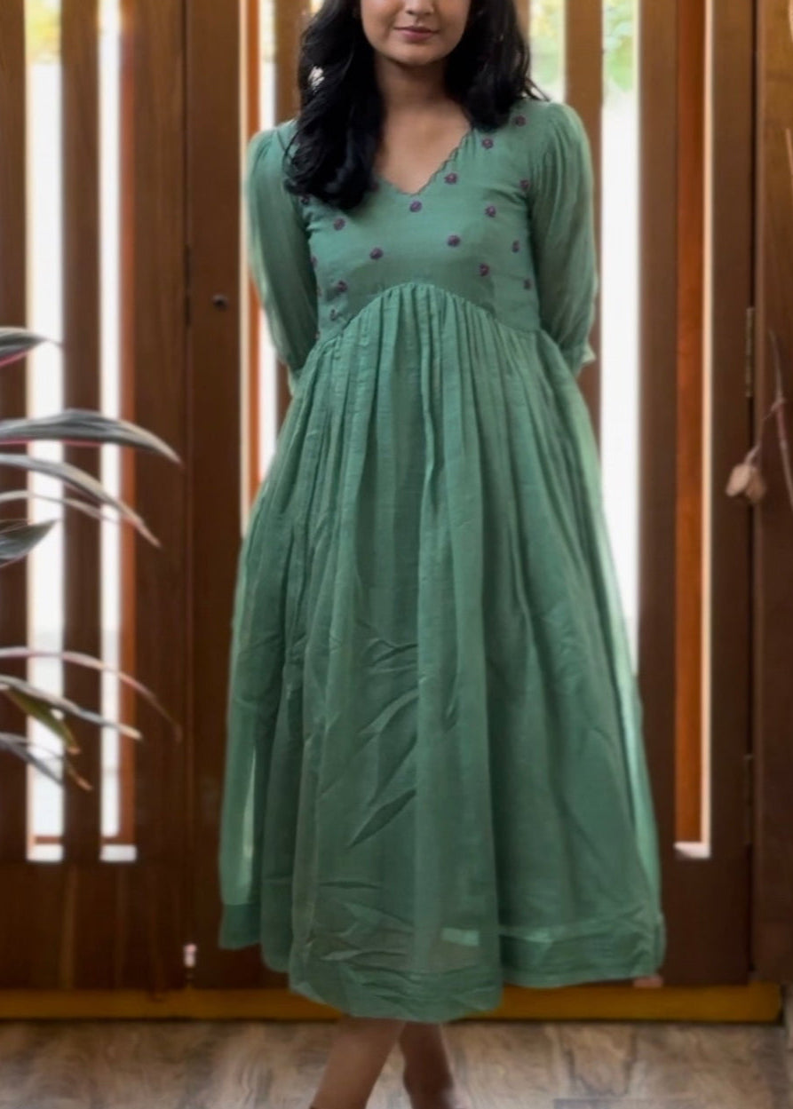 Woman in a green dress standing in front of a wooden panel door.