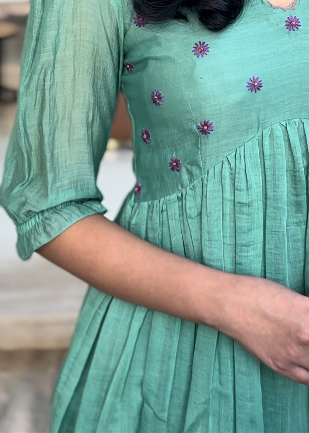 Green dress with floral embroidery worn by a person, blurred background