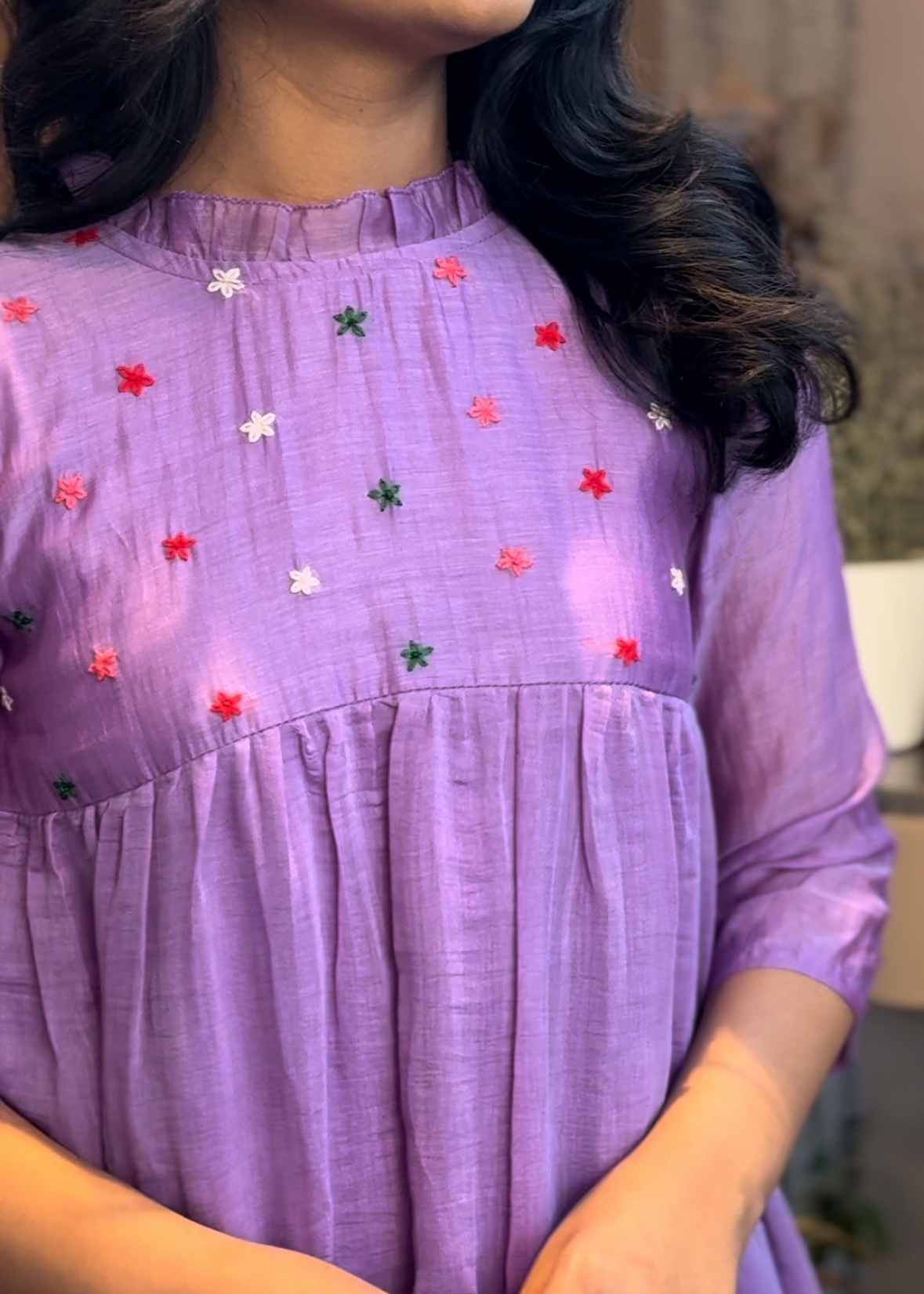 Person wearing a purple dress with floral embroidery