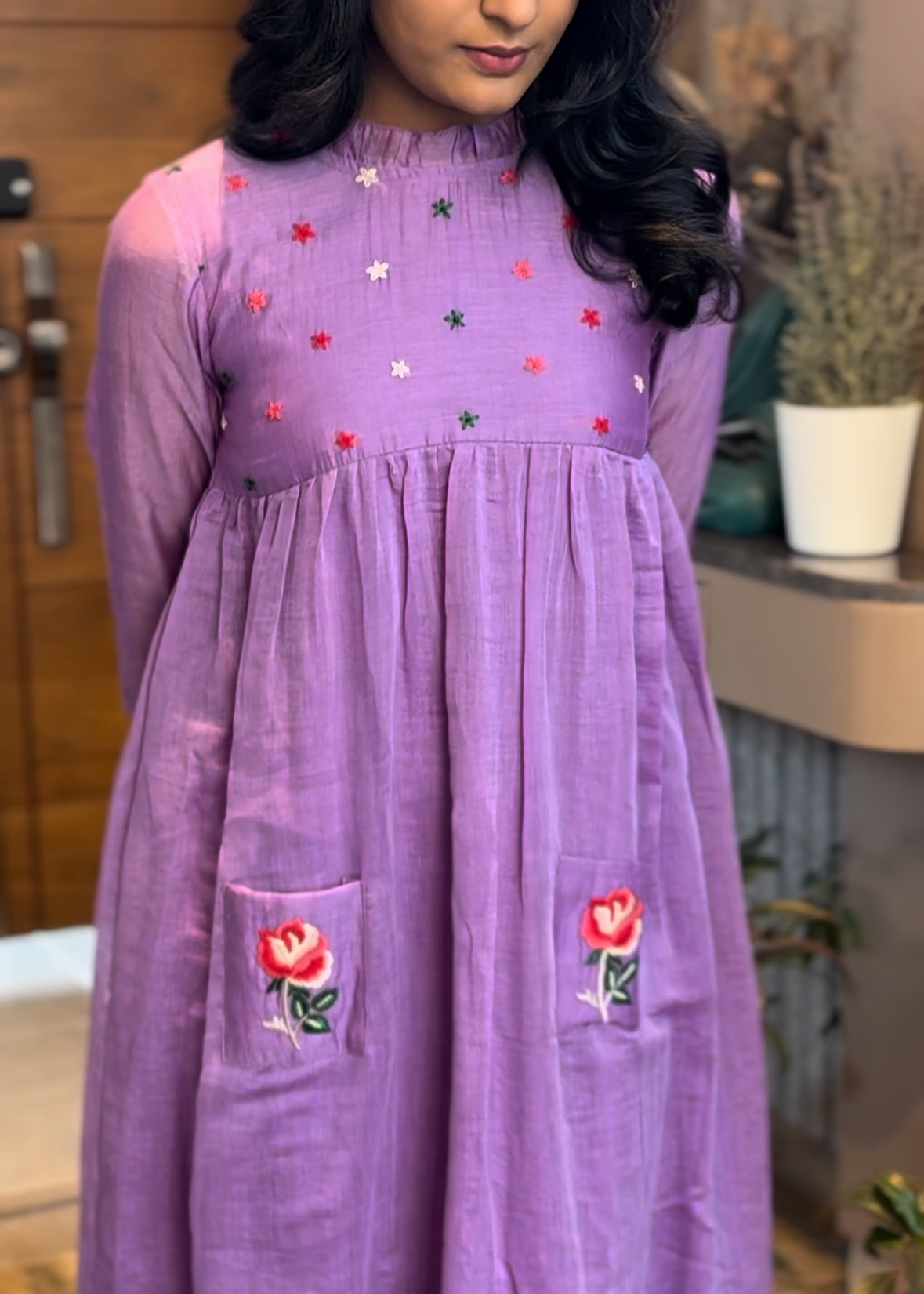 Woman wearing a purple dress with floral designs indoors.