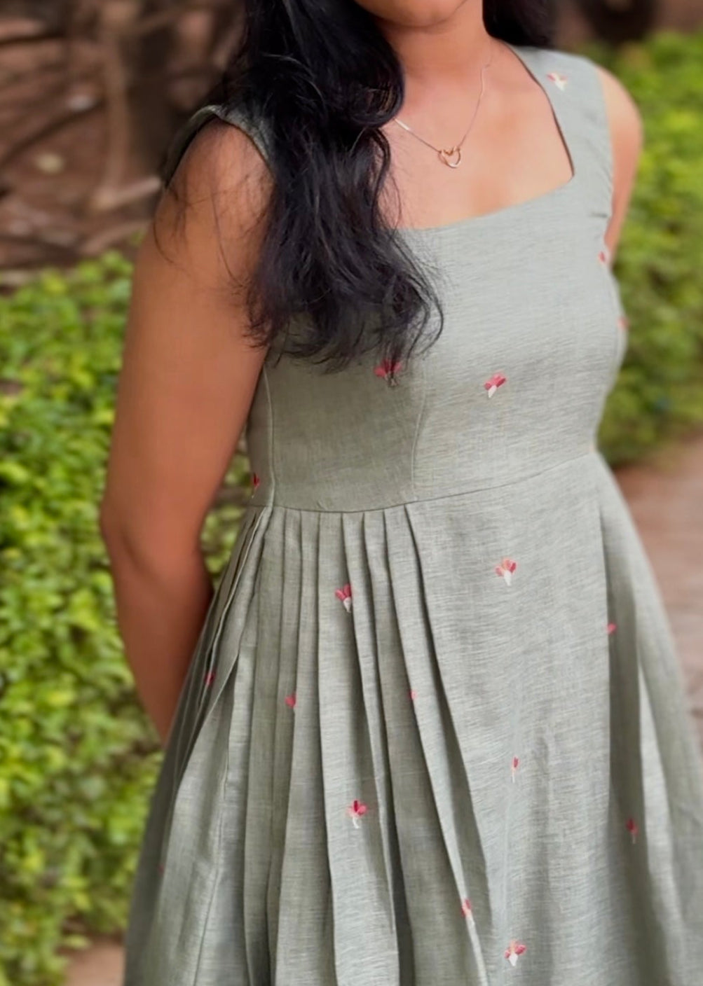 Woman in a light green dress standing outdoors with greenery in the background