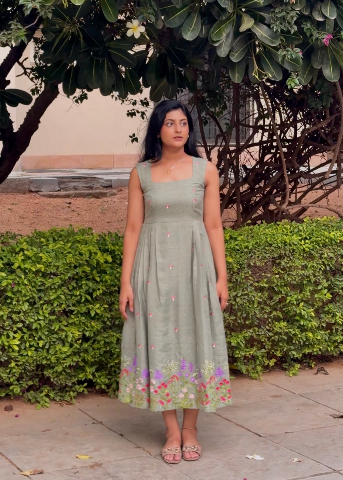 Woman in a green dress standing outdoors with trees and bushes in the background