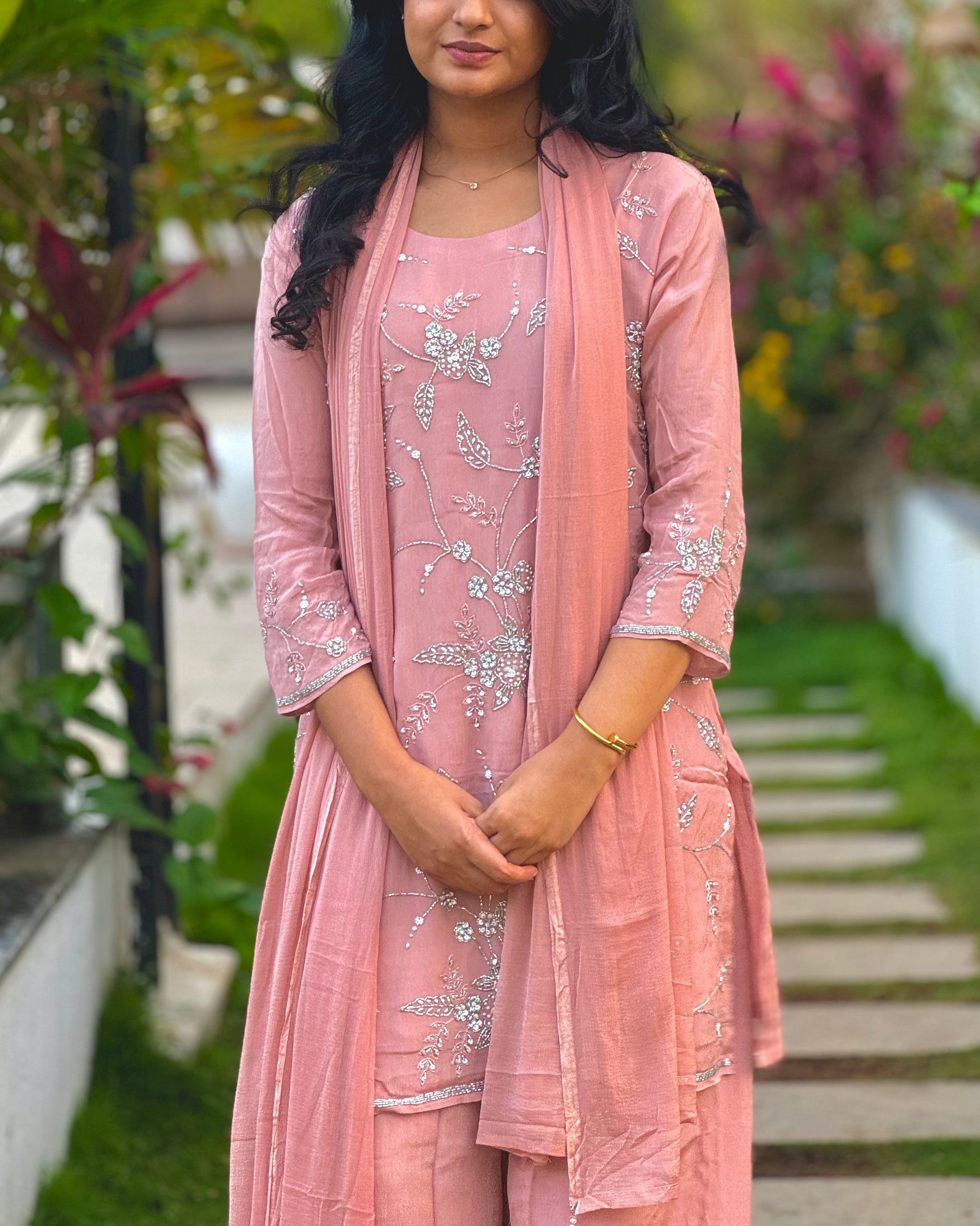 Woman wearing a pink traditional outfit with floral patterns in an outdoor setting.