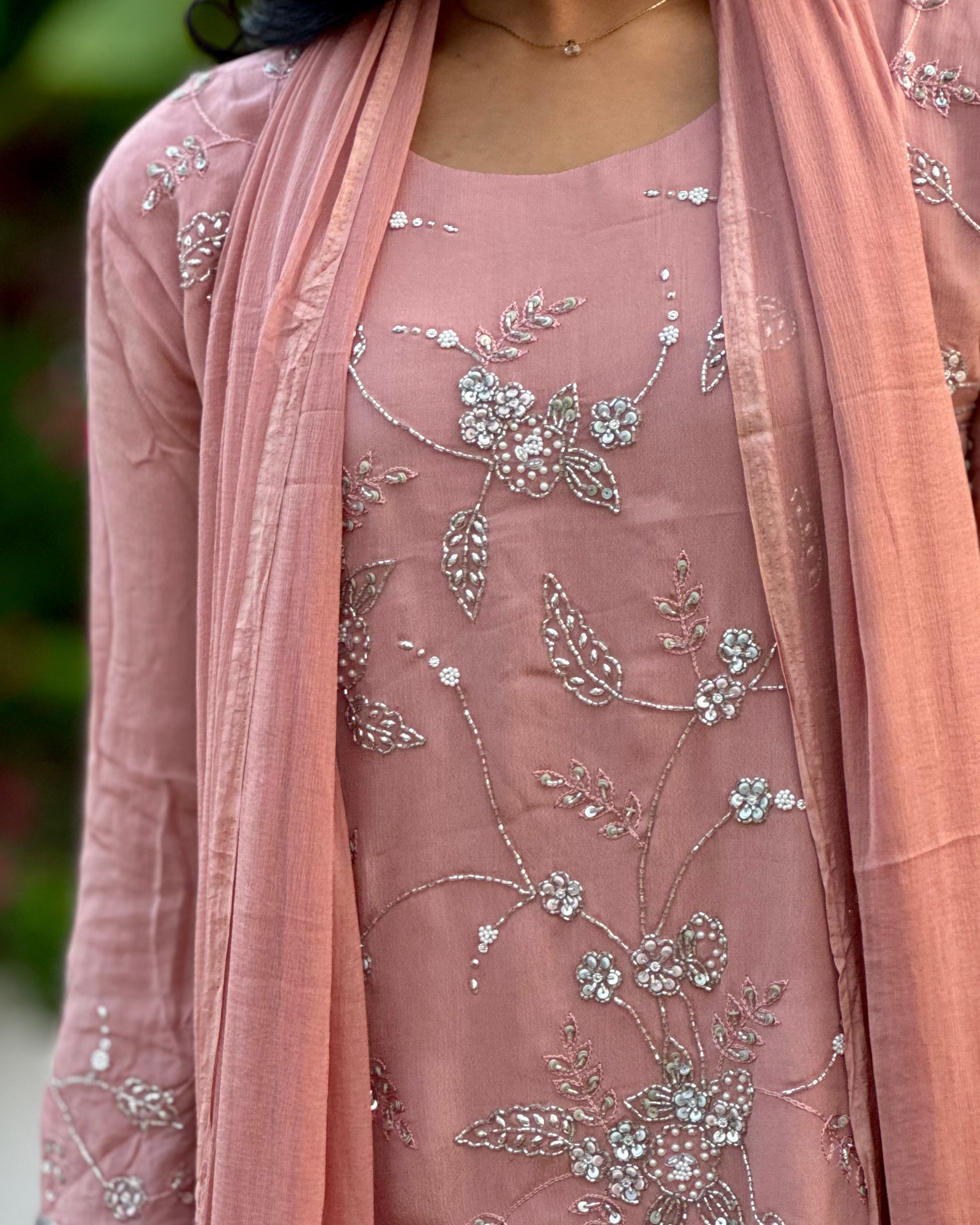 Pink embroidered outfit with a matching dupatta against a blurred green background