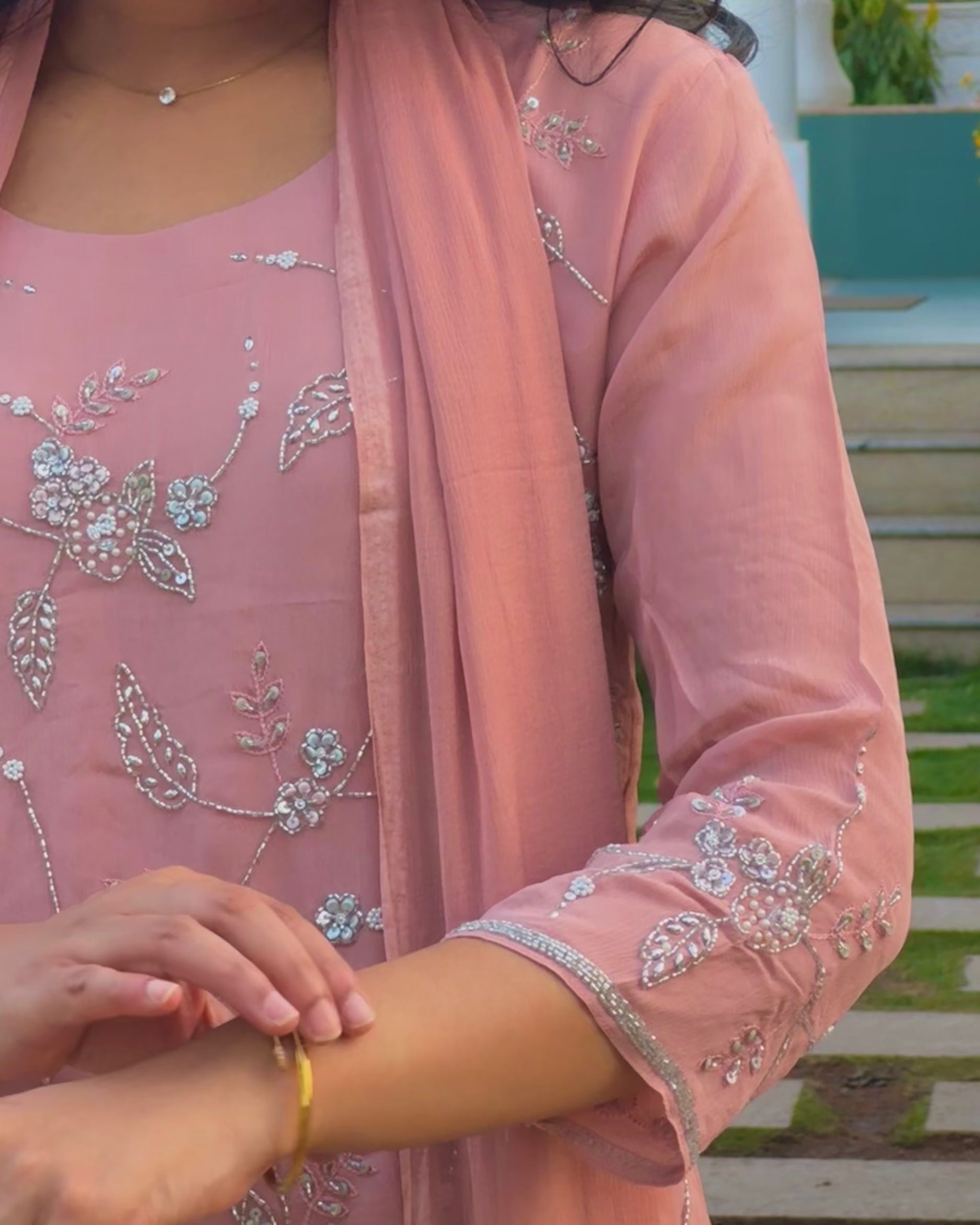 Close-up of a person wearing a pink embroidered outfit with a blurred outdoor background
