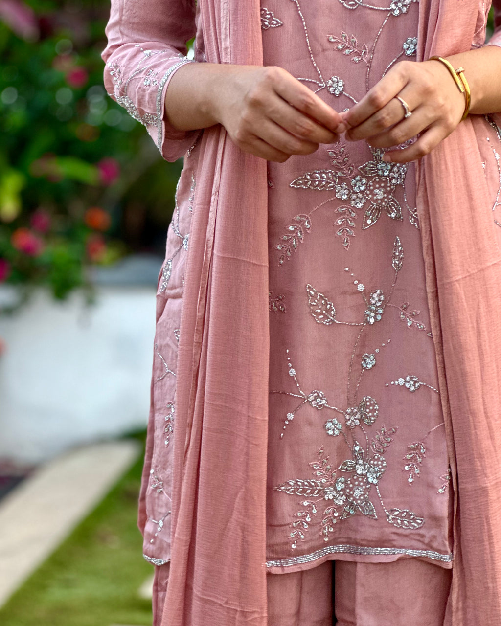 Pink embroidered traditional outfit with floral patterns, worn by a person.