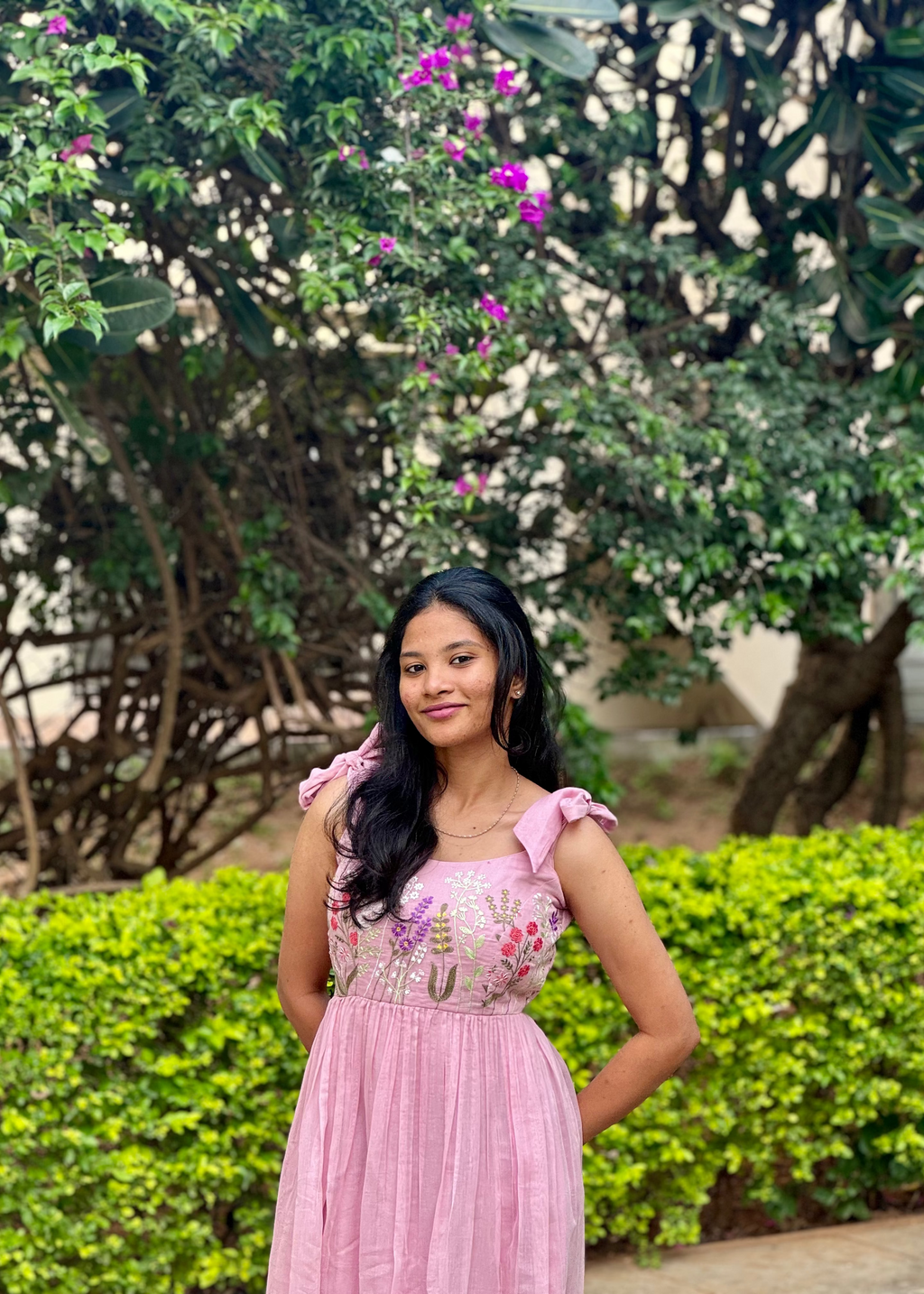 Woman in a pink dress standing outdoors with greenery and flowers in the background