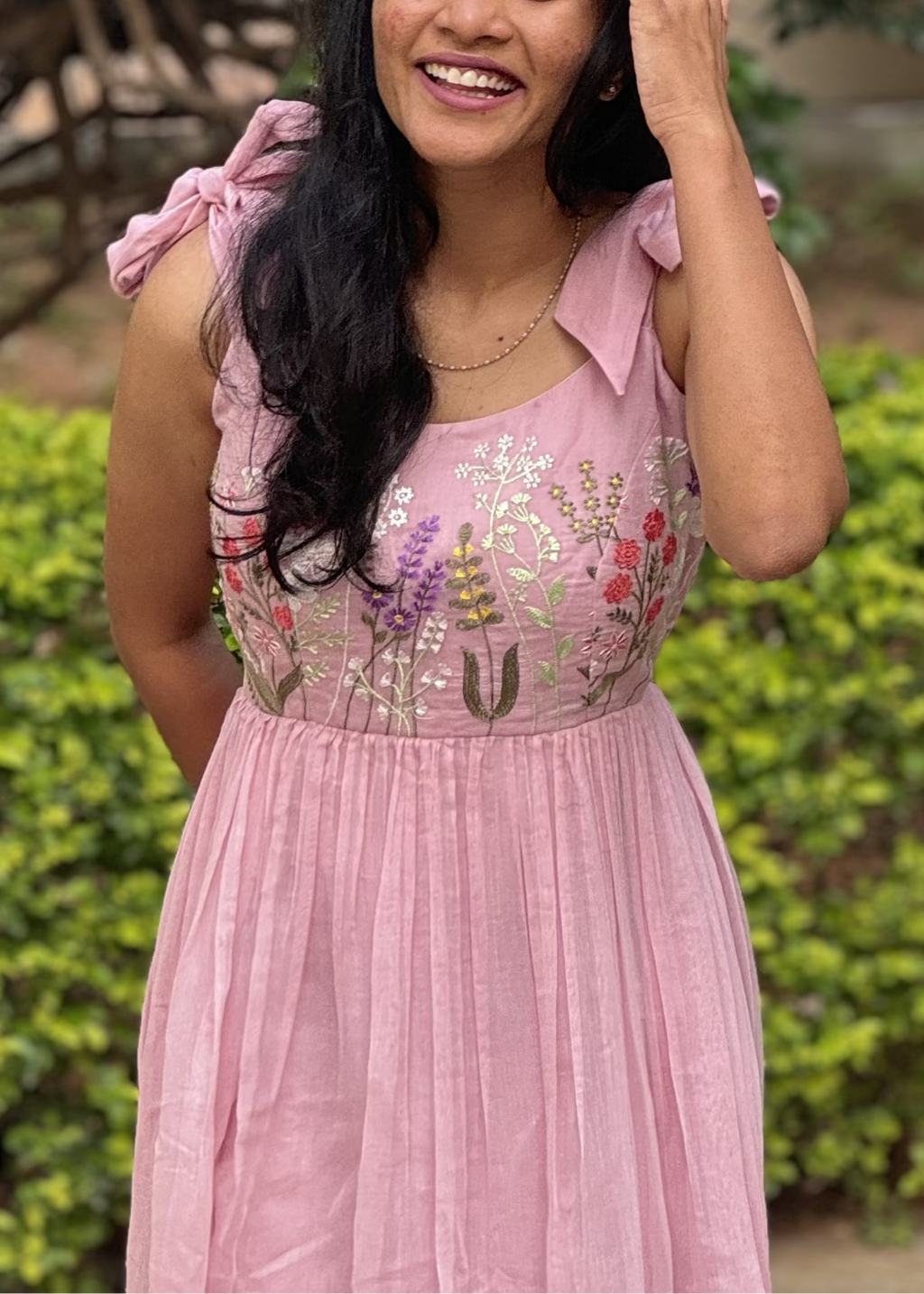Woman in a pink dress standing outdoors with greenery in the background