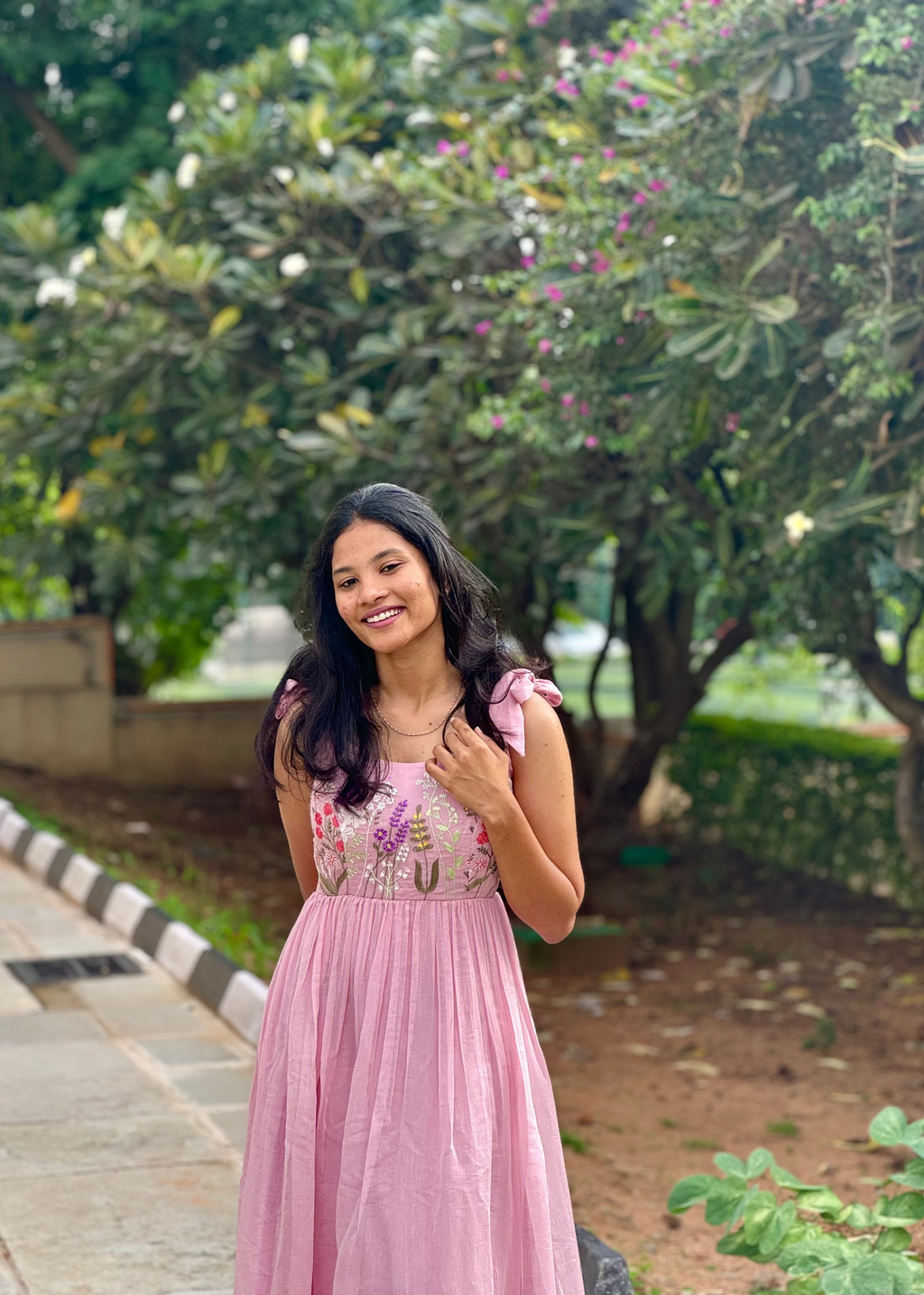 Woman in a pink dress standing outdoors with greenery in the background