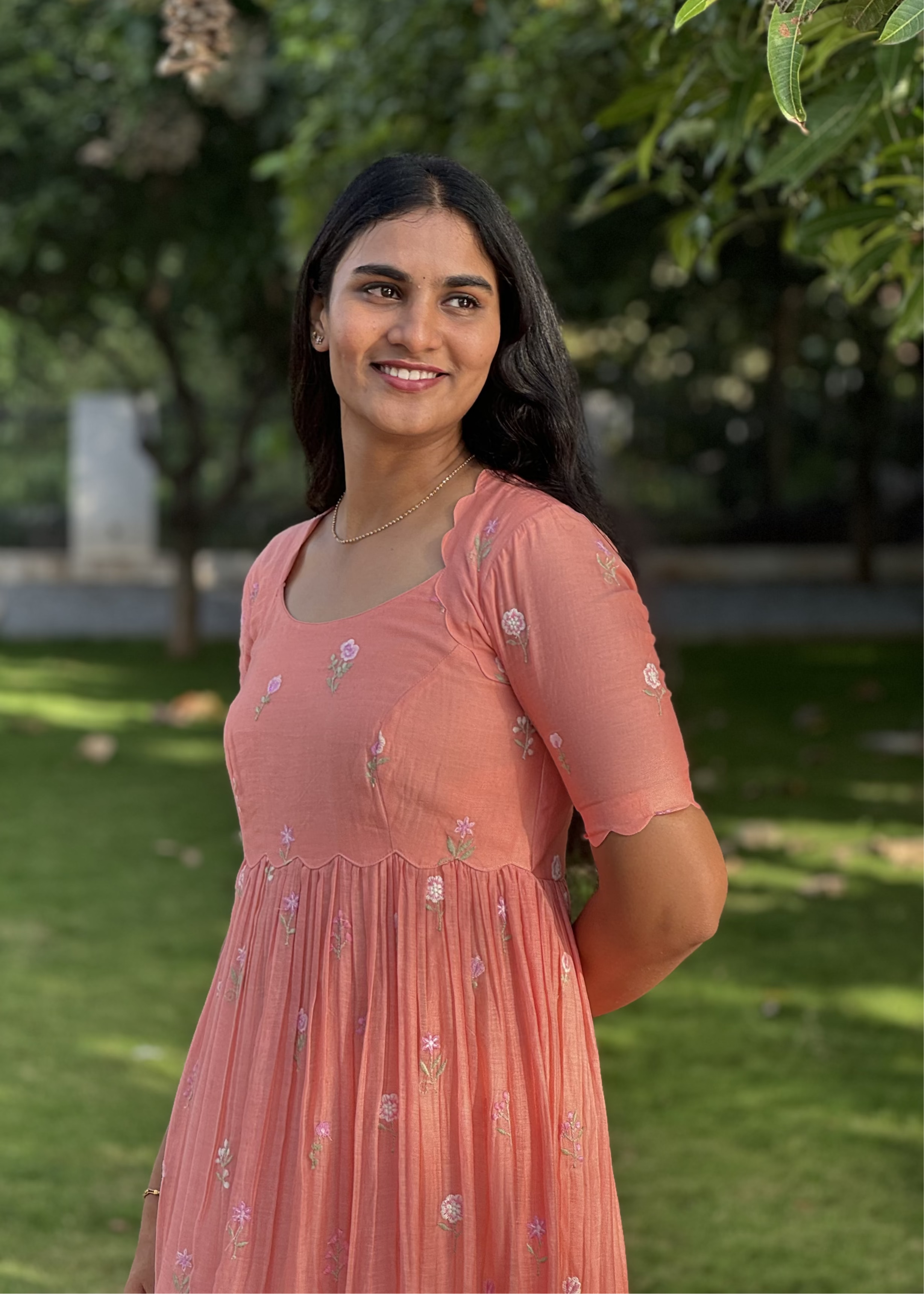 Woman in a peach dress standing outdoors with greenery in the background