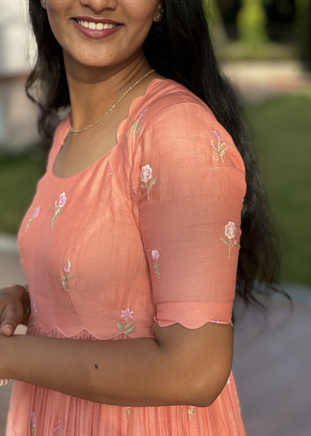Woman wearing a peach-colored dress with floral embroidery outdoors