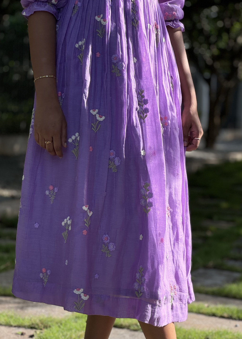 Person wearing a purple dress with floral patterns outdoors.