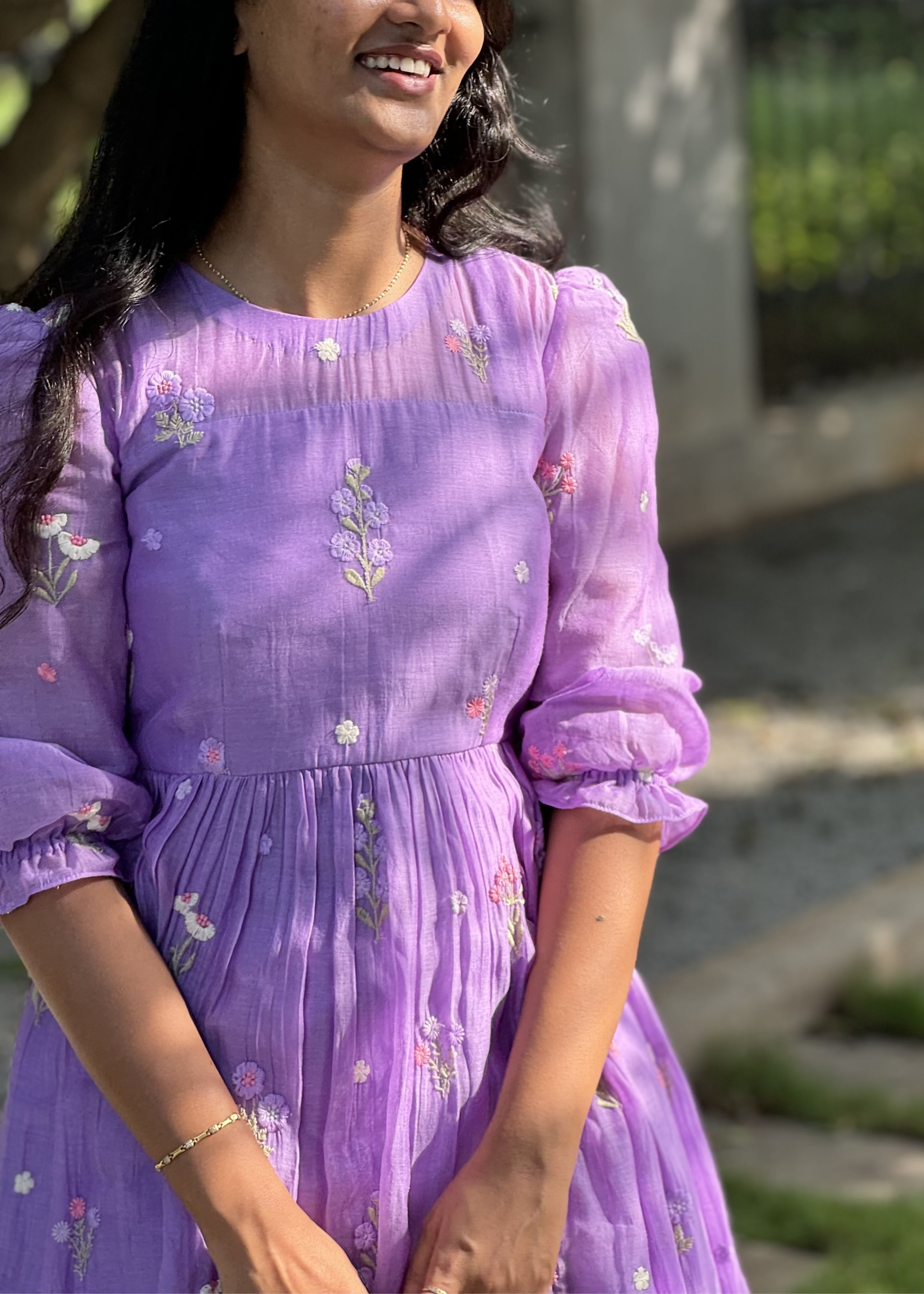 Woman wearing a purple dress with floral patterns outdoors.