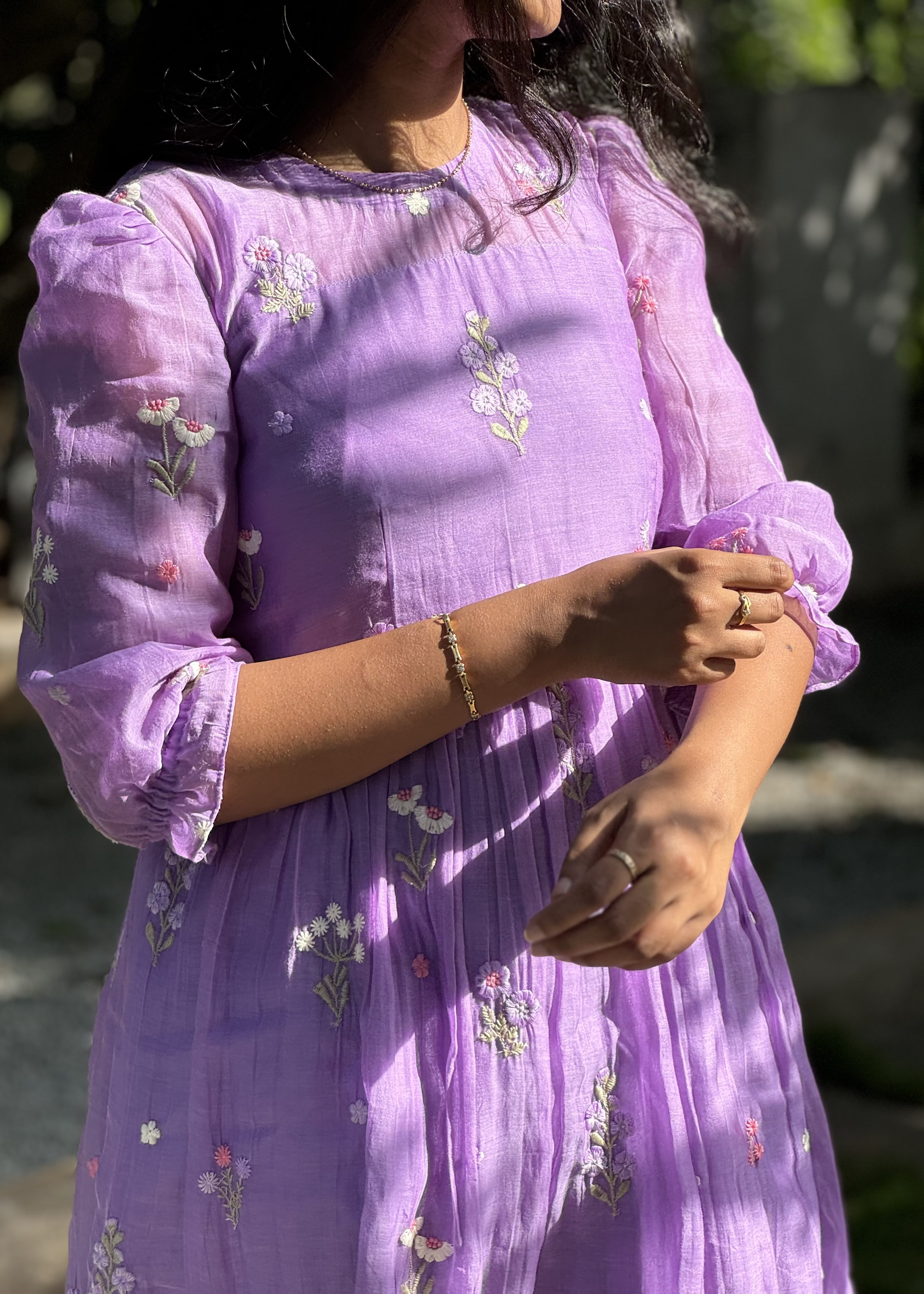 Person wearing a purple dress with floral embroidery in an outdoor setting